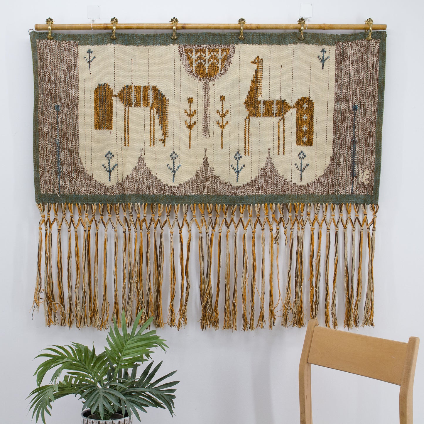 Close up of the warm earthy tapestry beautifully styled on a bright wall, displaying the woven horse motifs over long handmade macrame fringes.