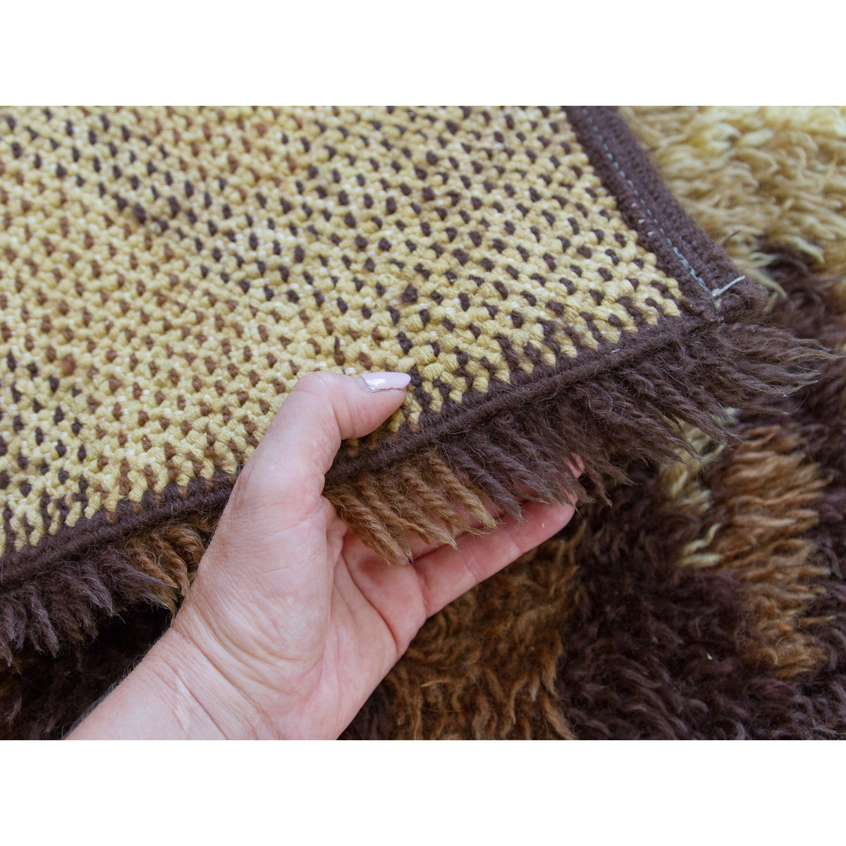 Hand lifting the edge of a vintage shag rug to show both the strong backing and the soft long piles