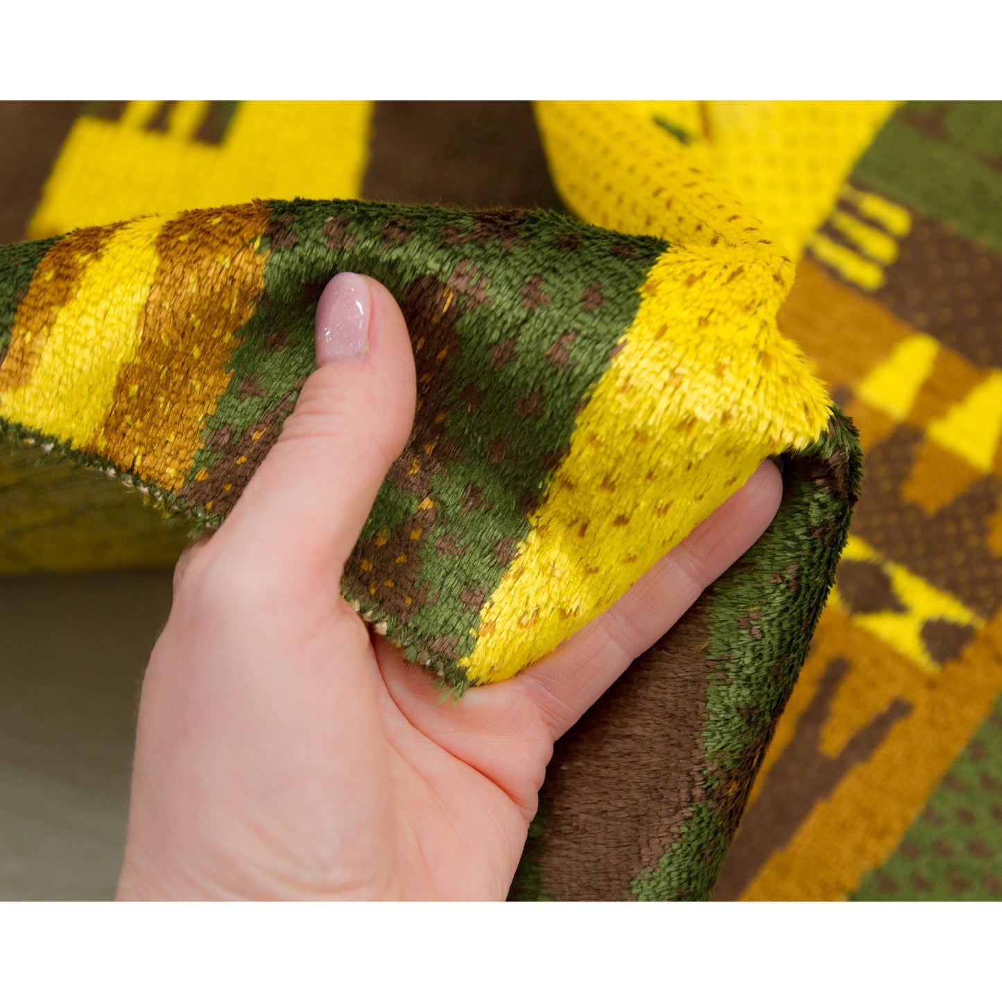 Hand squeezing the soft, thick pile of the tapestry. A sensory decor piece that adds warmth and acoustic dampening to a room.