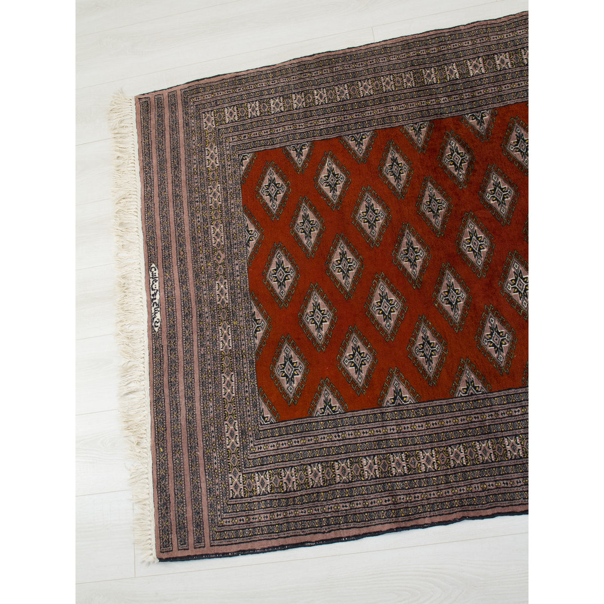 Angled top view of signed Bokhara rug with rows of diamond Turkoman guls on rust red field