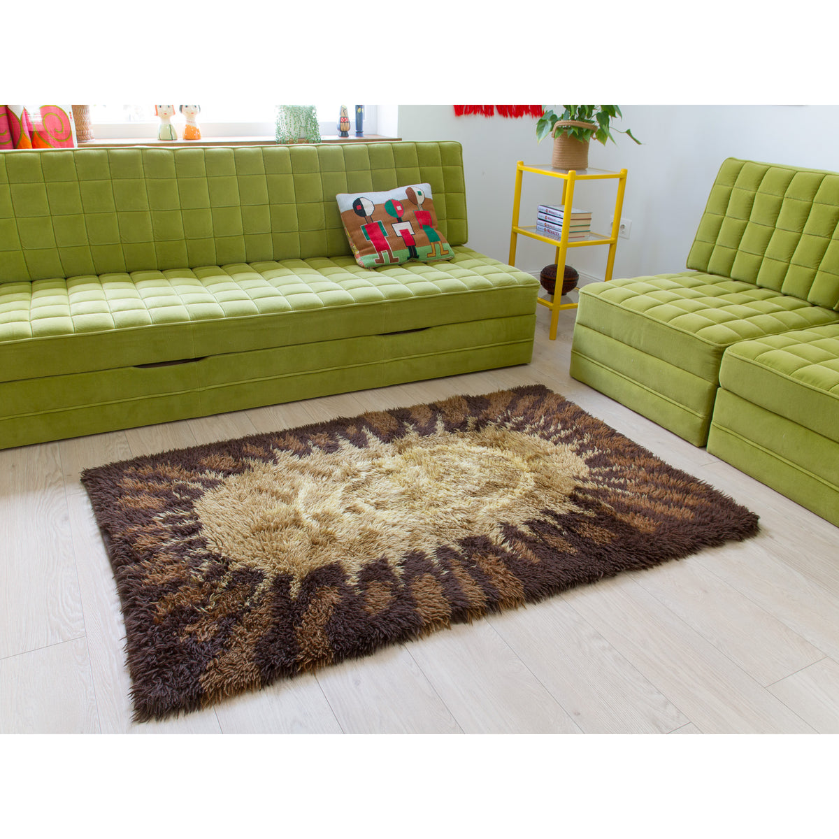 A 70s vintage shag area rug with a brown and beige sunburst pattern, shown in a retro - mid century style living room setting with lime green tufted sofas.