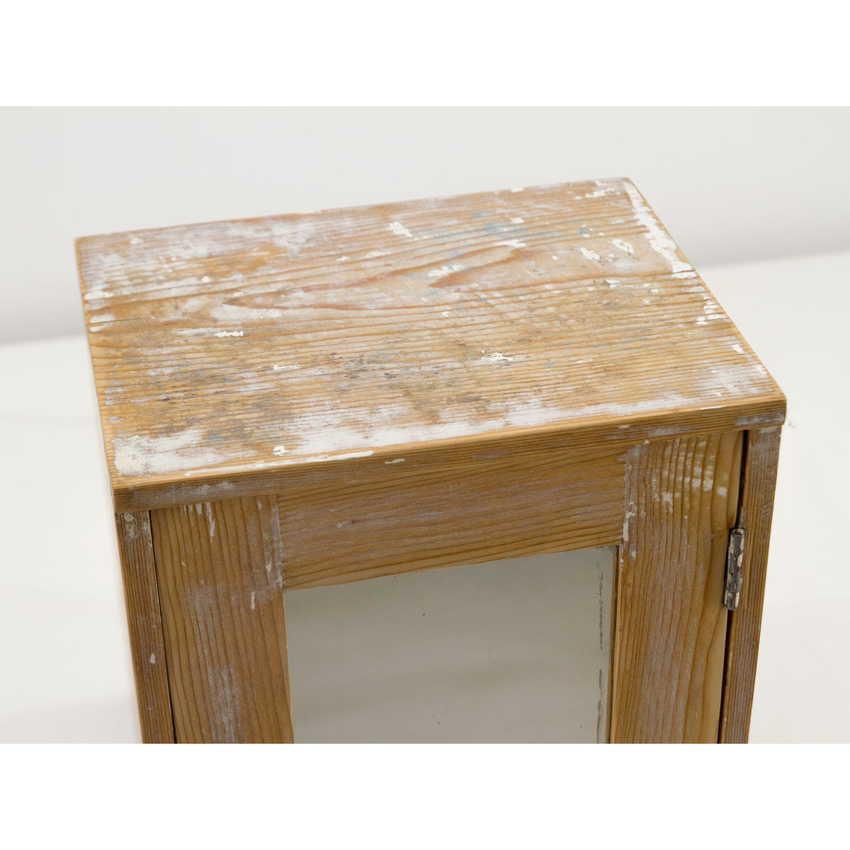 Angled view of the top of the small vintage wooden wall cabinet. Rustic farmhouse or French cottage style furniture with a distressed white paint finish, showing the natural wood grain and weathered texture.