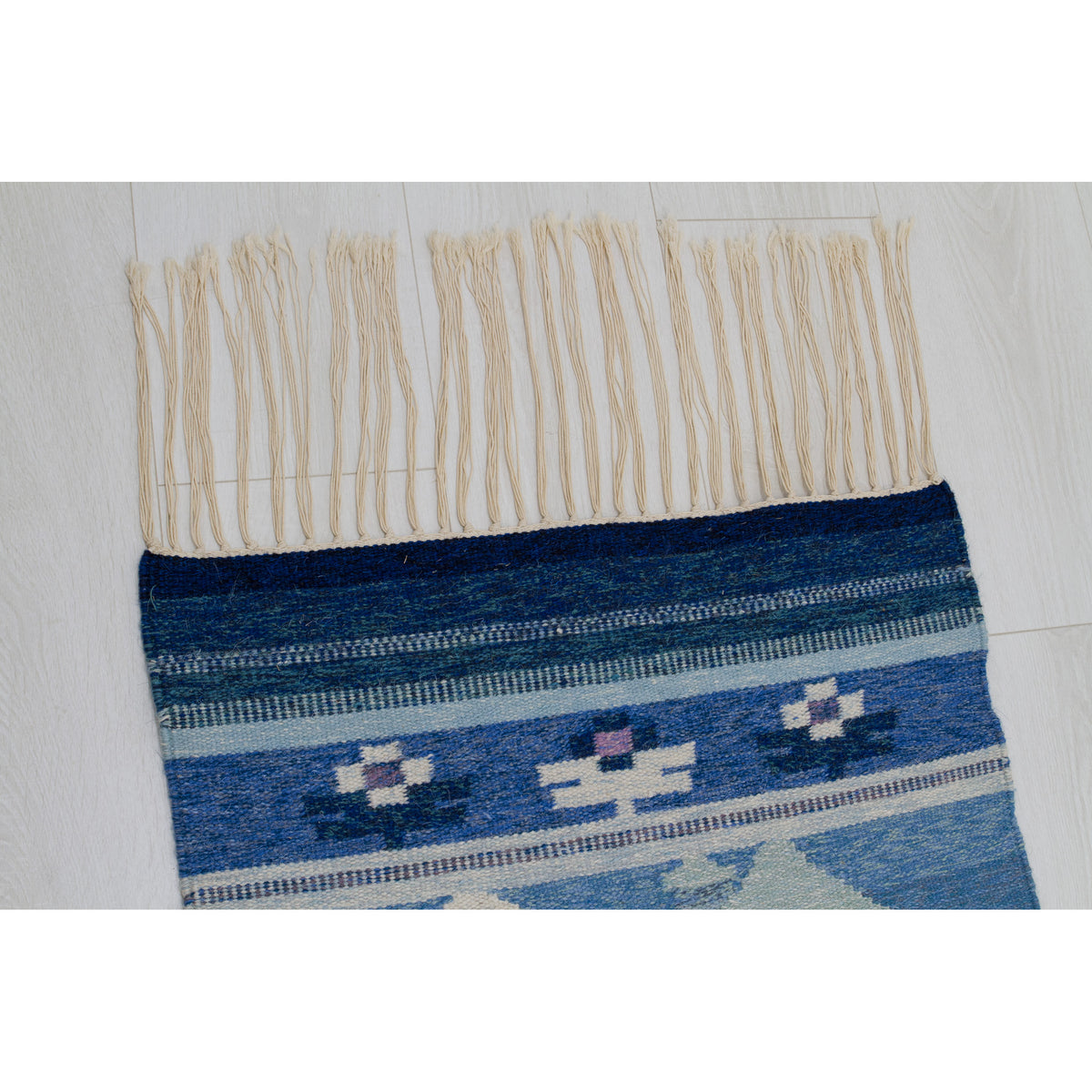 Close up of the cream wool fringe. The fringe is approximately 6 inches long and is present on both the top and bottom of the rug.