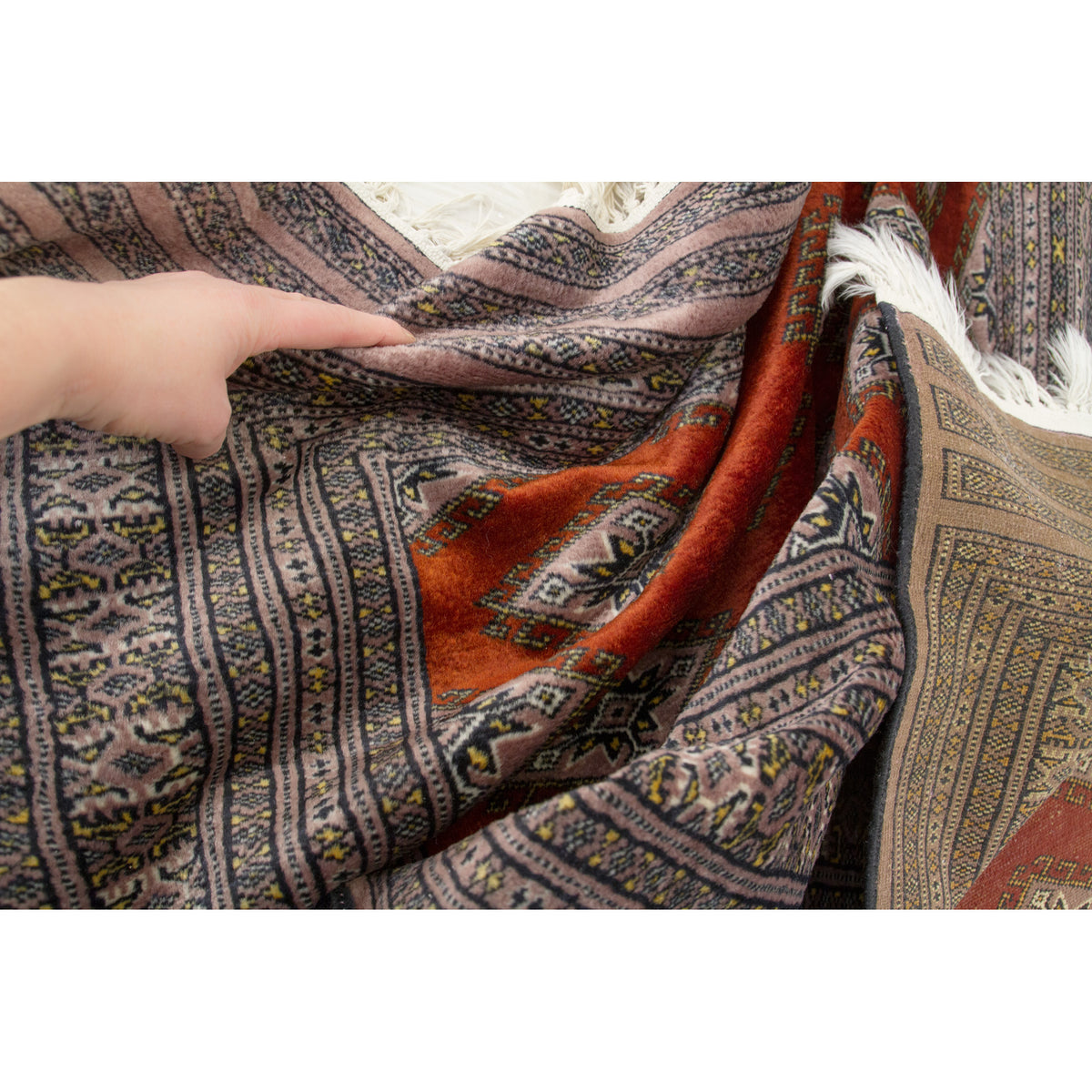 Hand touching the soft draped border of a vintage silk rug, back side visible on the right
