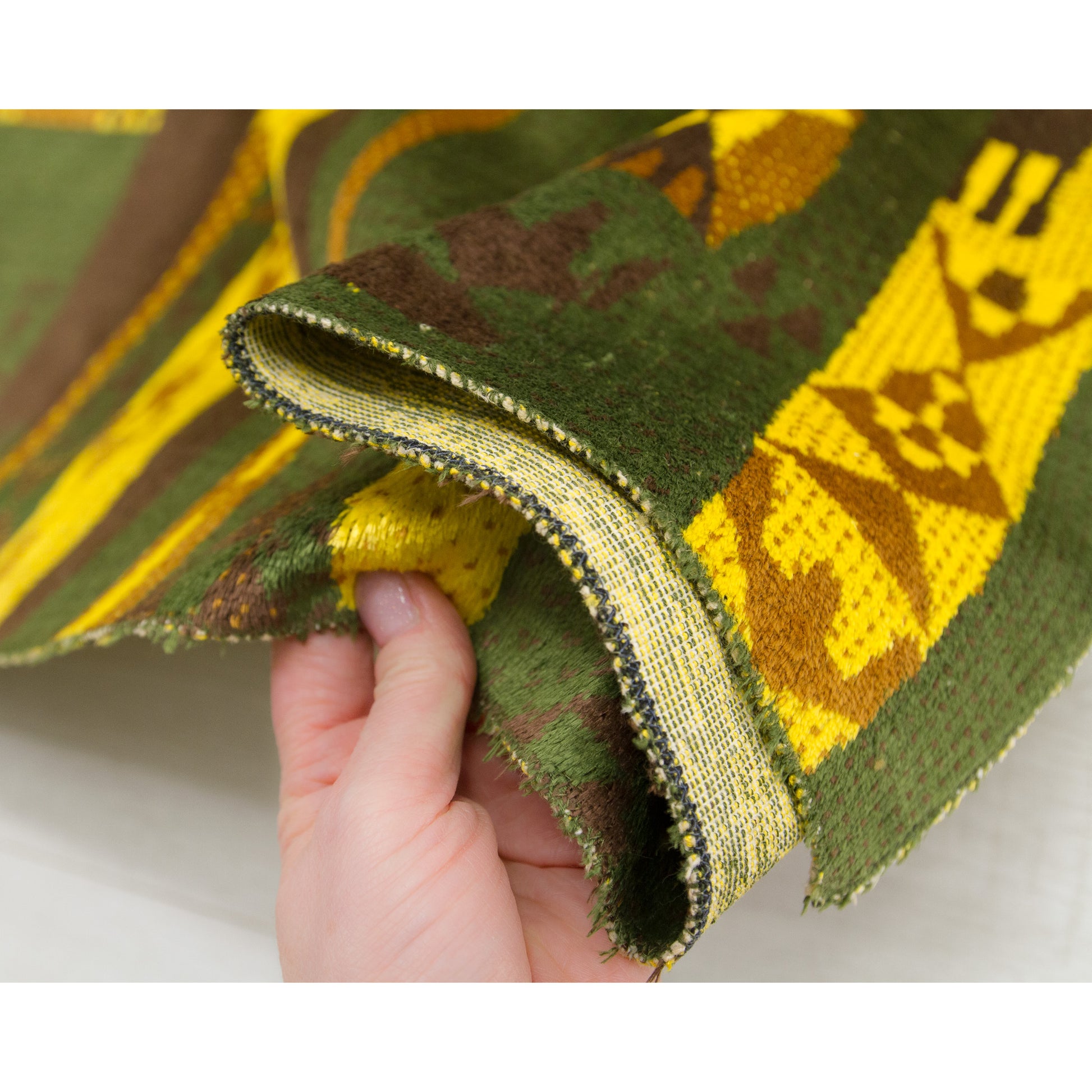 Closeup of the soft tapestry fabric, held in hand, to demonstrate the structure of the  high quality textile and serged edges.