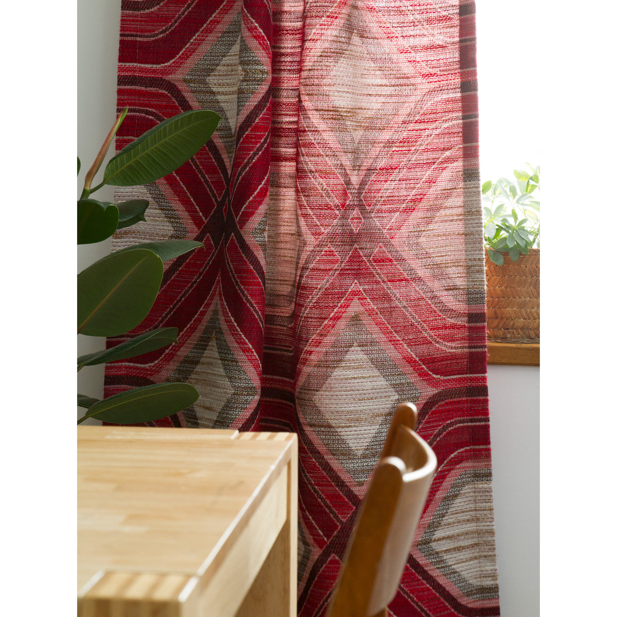 Space Age geometric curtain in red, pink and grey with plant, table and wooden chair, decorating a vintage - retro style home