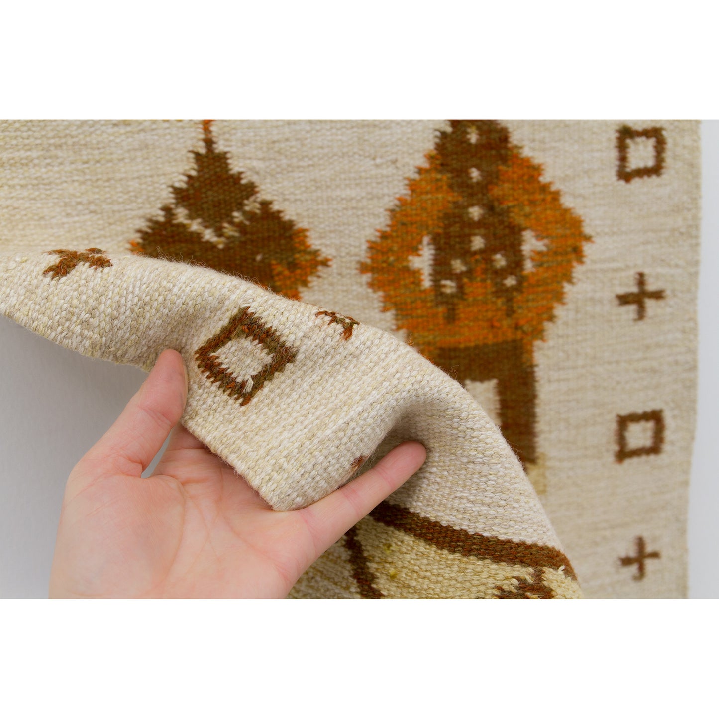 A hand gently bending the edge of the woven fabric to display the sturdy, pliable wool-on-cotton-warp texture and excellent European cottage craftsmanship.