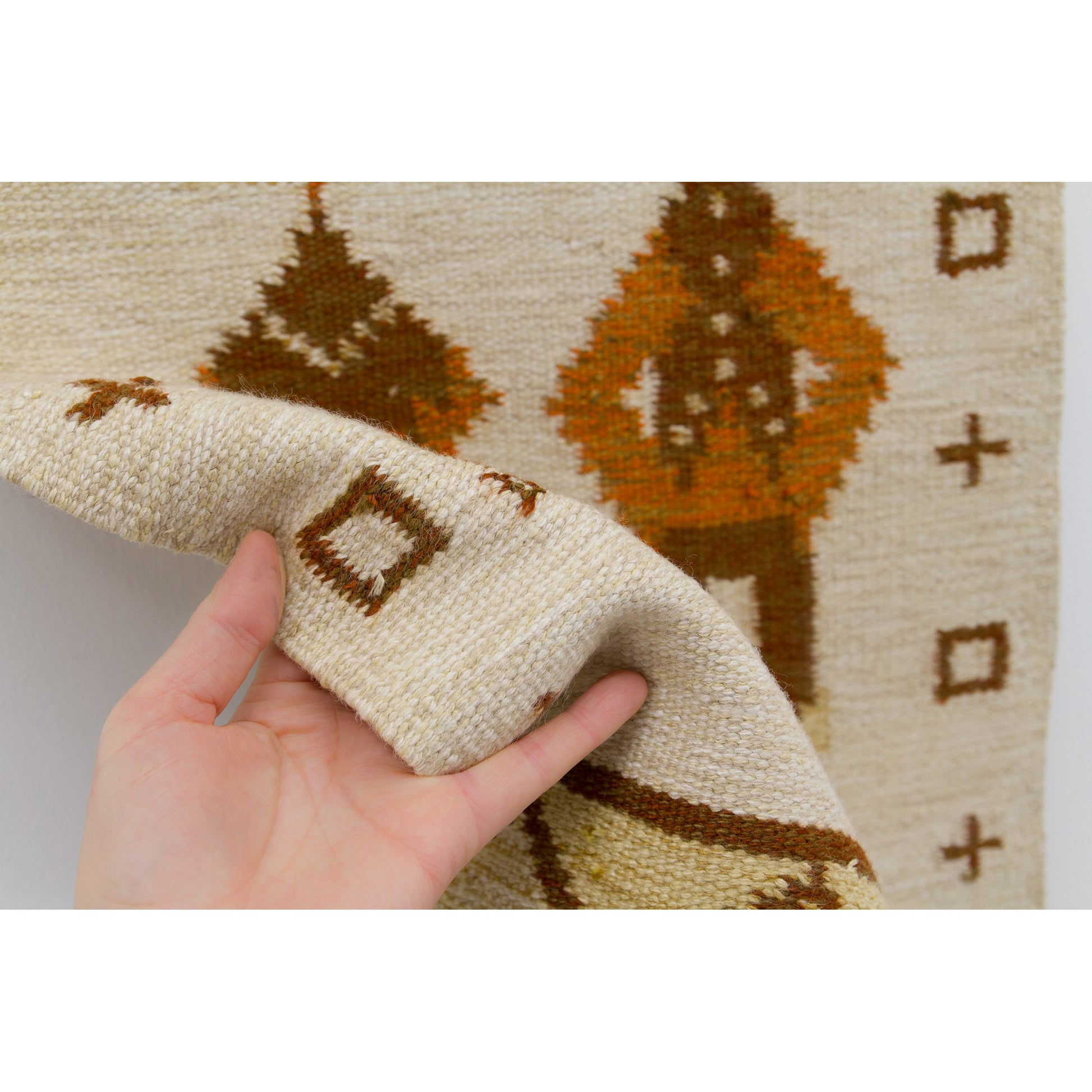 A hand gently bending the edge of the woven fabric to display the sturdy, pliable wool-on-cotton-warp texture and excellent European cottage craftsmanship.