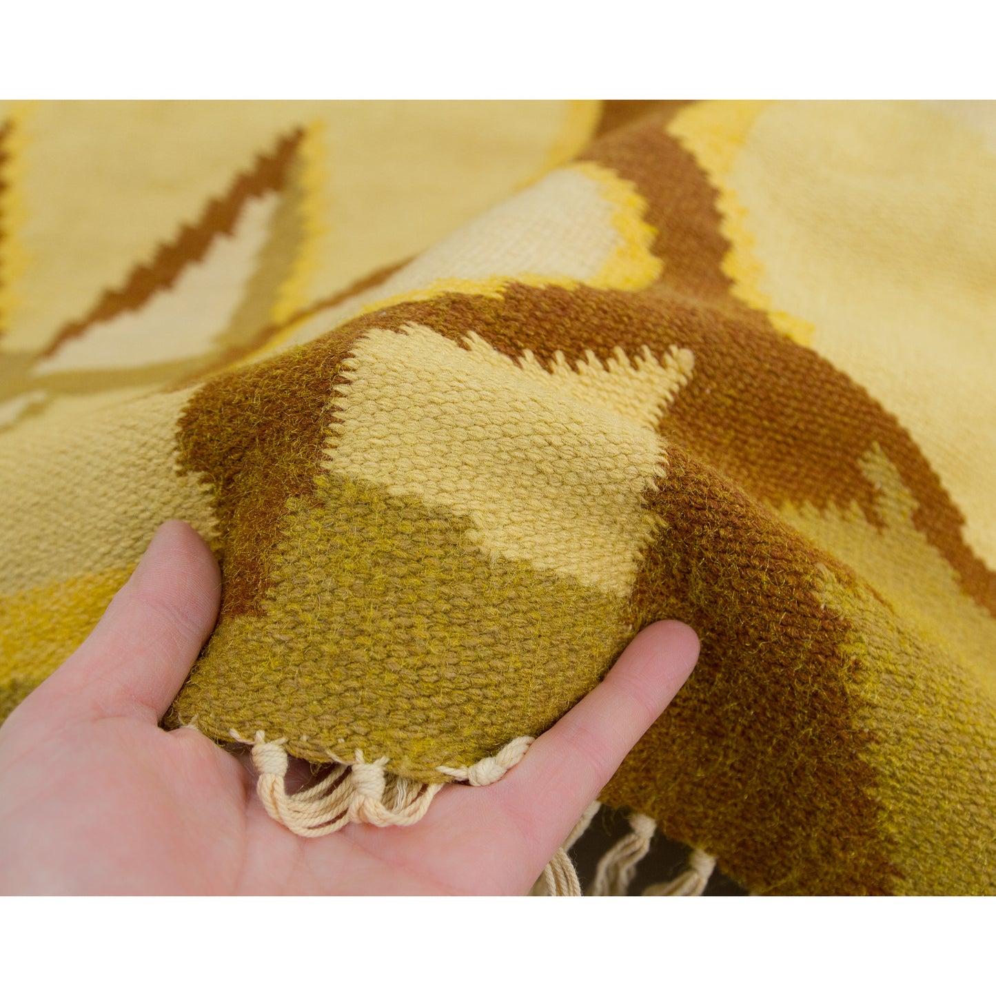 Fingers grasping the textile's side edge to visually communicate how tightly woven, pliable, and substantial this classic 70s home accessory feels in person.