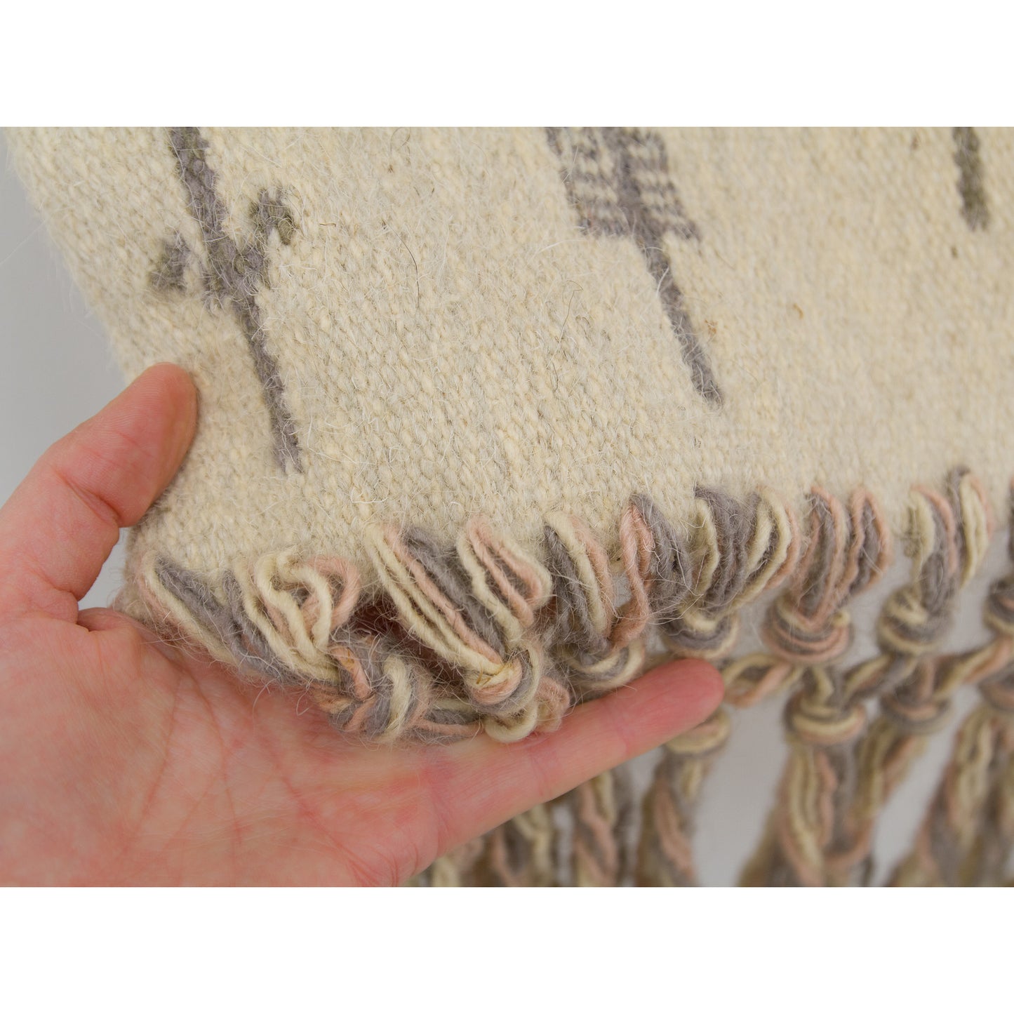 Hand gently supporting the tapestry where the flatweave connects to the intricate macrame tassels, revealing the highly skilled mid-century craftsmanship of the artisan weavers.