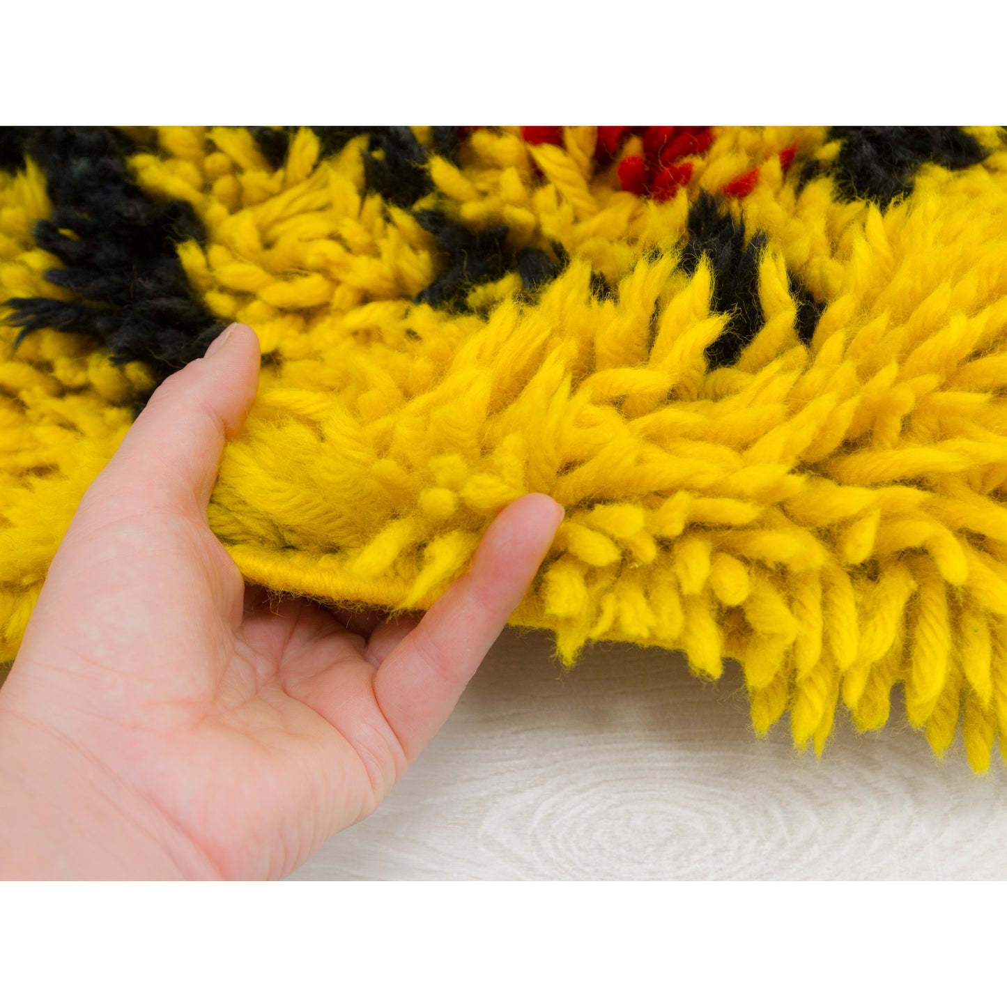 Hand lifting the edge of the vintage yellow tapestry rug, displaying its heavy-weight structural integrity and thick woven base, along with the extra high, thick piles.