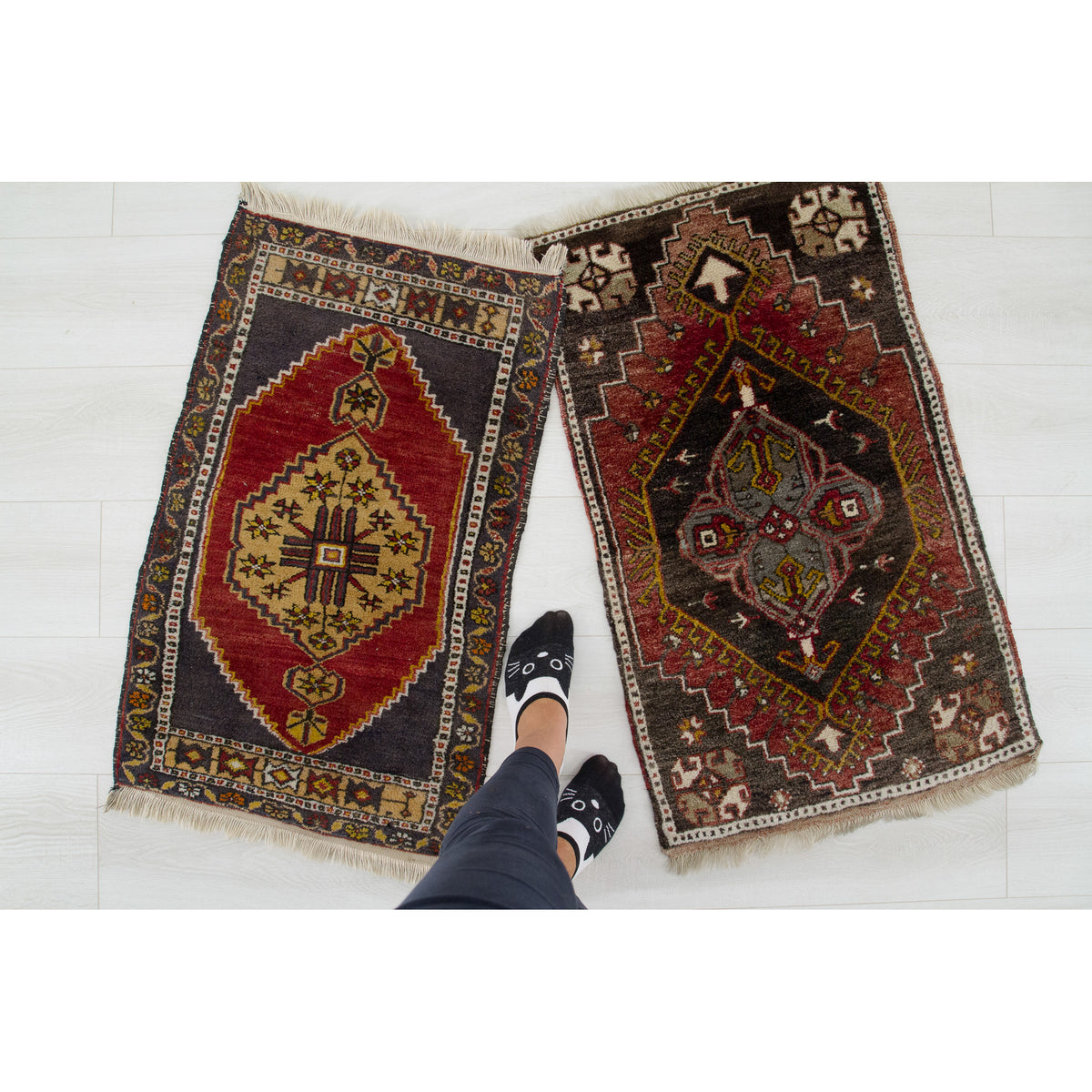 Two small hand-knotted vintage rugs on a white floor, with feet next to them to show the size