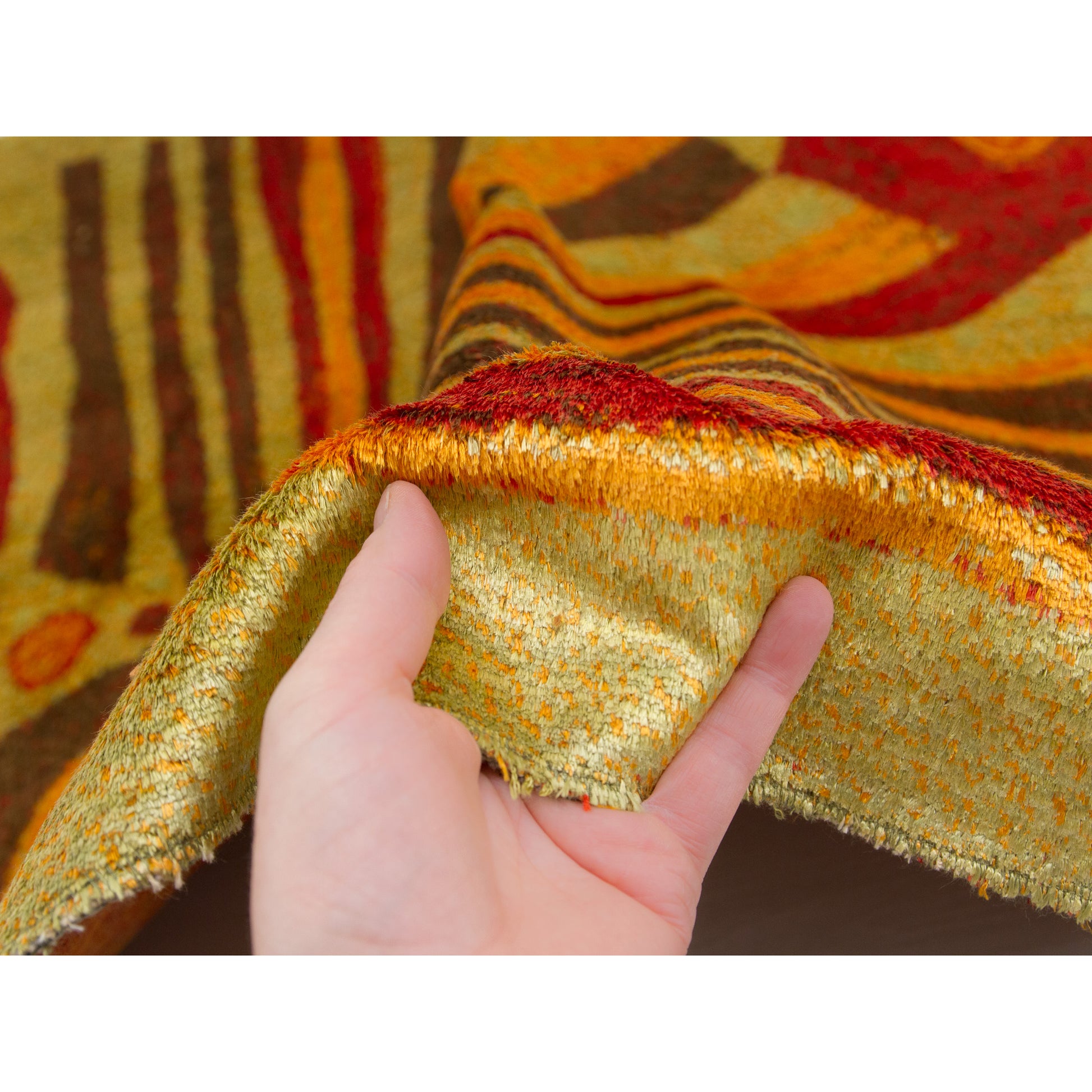 Hand holding the neatly hemmed edge of the tapestry, showing the gentle shimmering of the moquette pile fabric, along with the warm color combination that is so typical of the 1960s modern aesthetic.