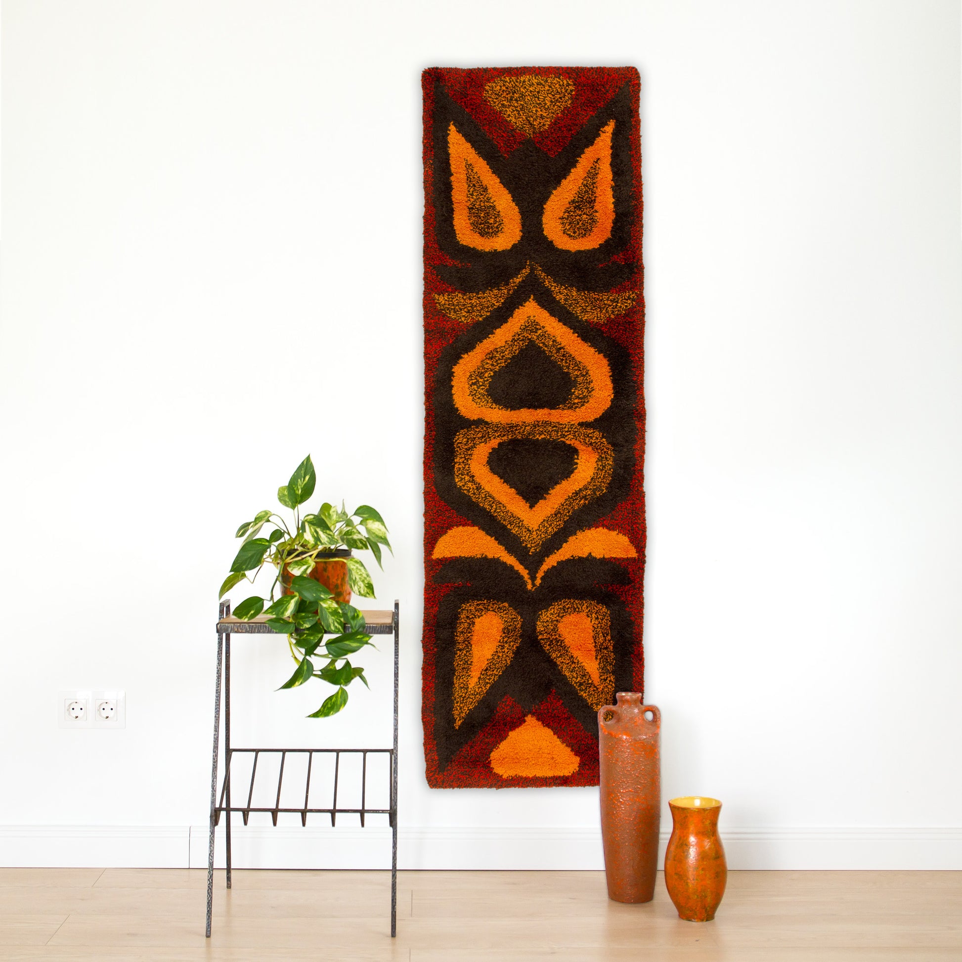The plush orange mid-century tapestry styled vertically on a narrow white wall behind a wooden side table, demonstrating versatile room styling.