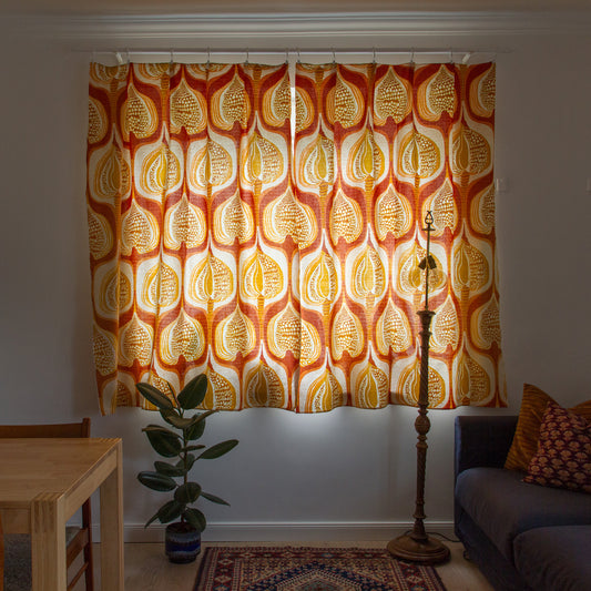 Pair of vintage 1970s orange and yellow cotton curtains hanging on a window in a cozy retro style living room