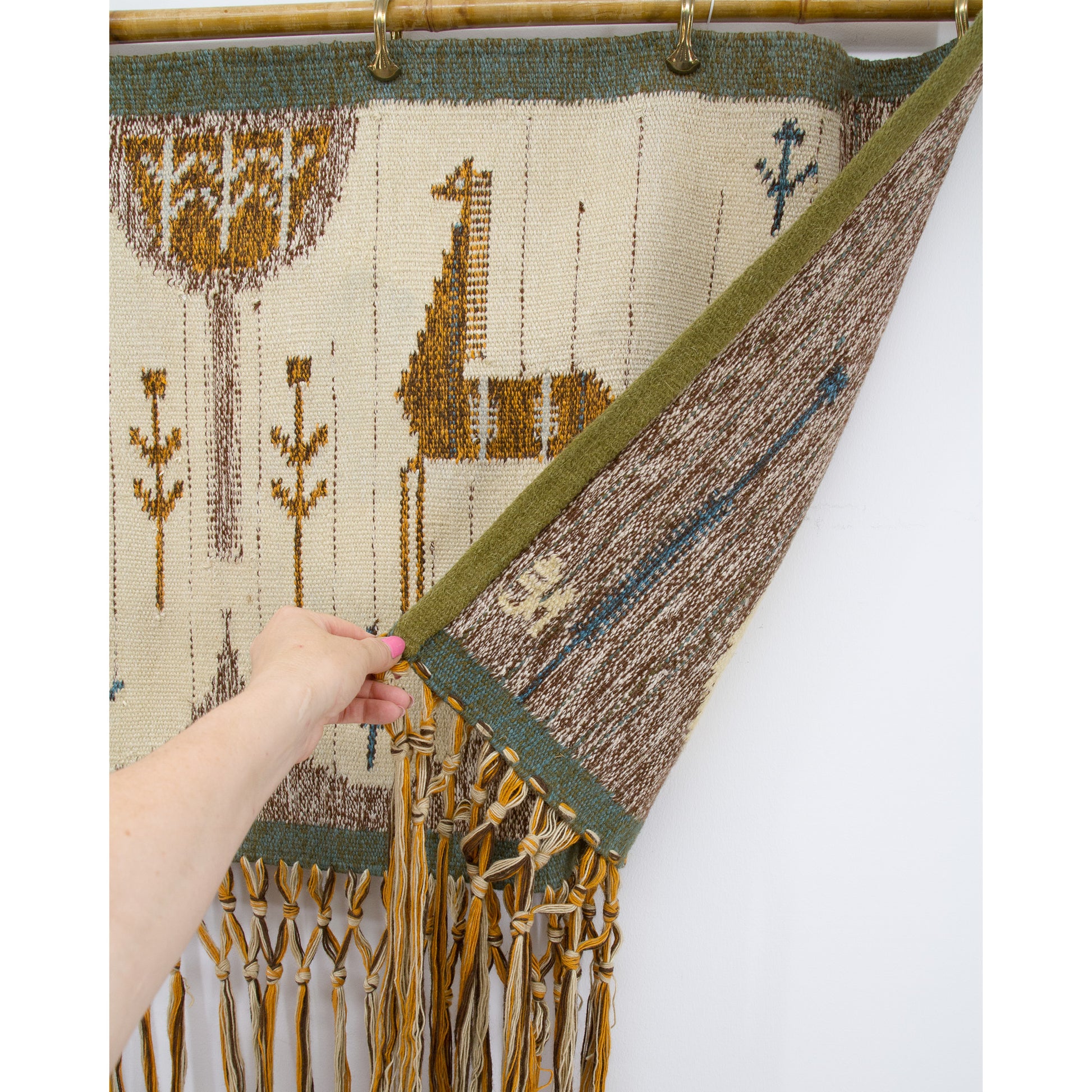 Hand peeling back one corner of the wool art piece to confirm the back side features matching colors, expert weaving, and excellent preserved condition.