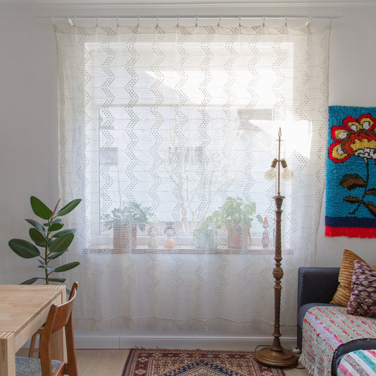 Large vintage crochet lace curtain in creamy white covering a sunny window in a boho living room