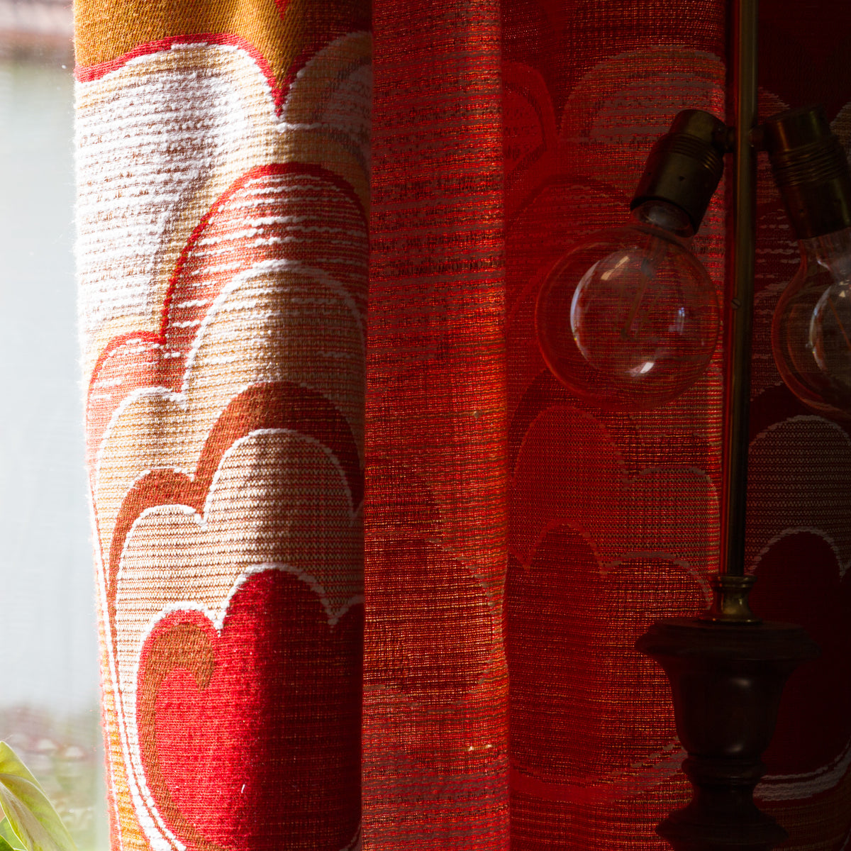 Vintage curtain glowing orange in backlight next to a brass lamp, showing the textured woven textile