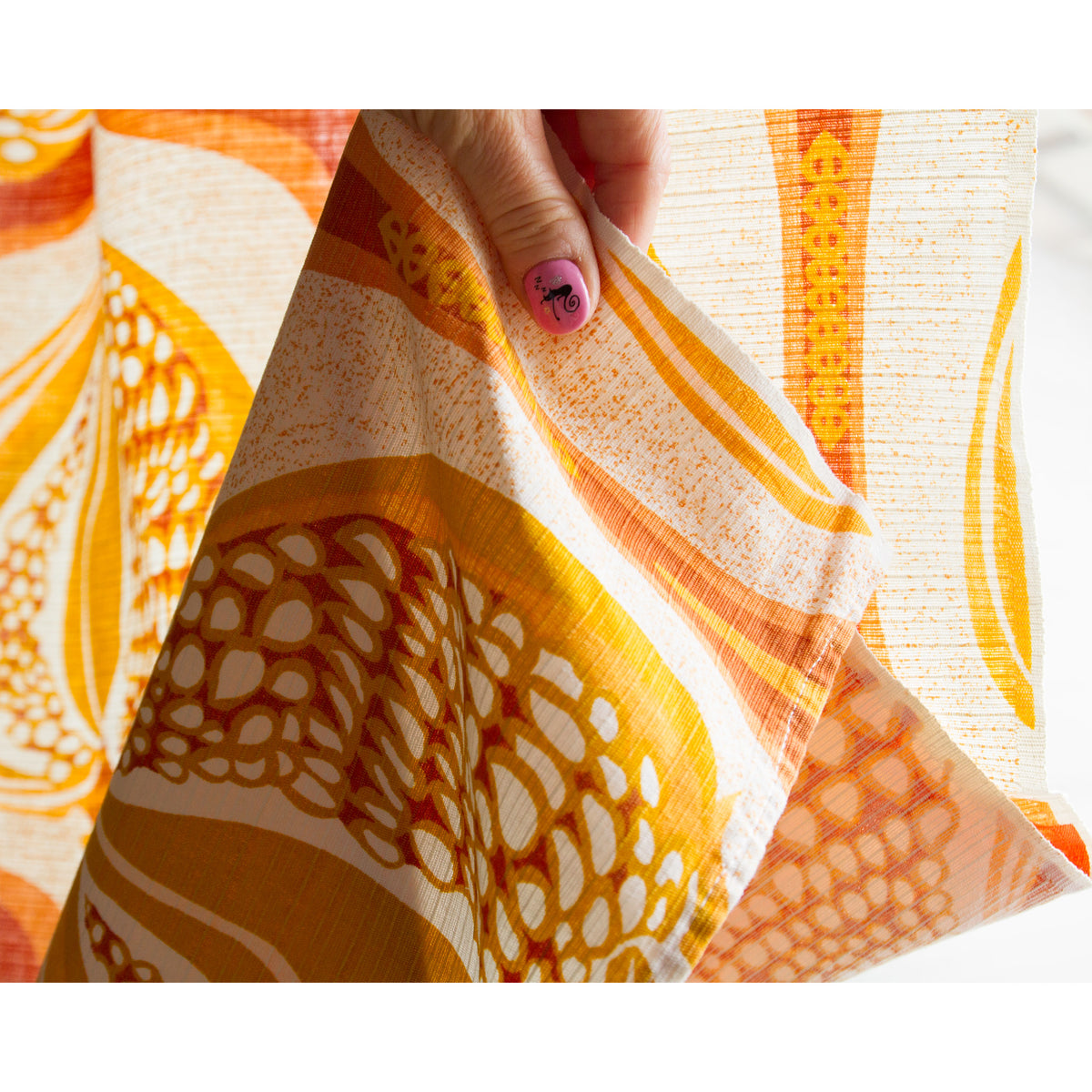 Folded corner of vintage cotton curtain showing front print and back side of the fabric, along with the neatly hemmed bottom edge.