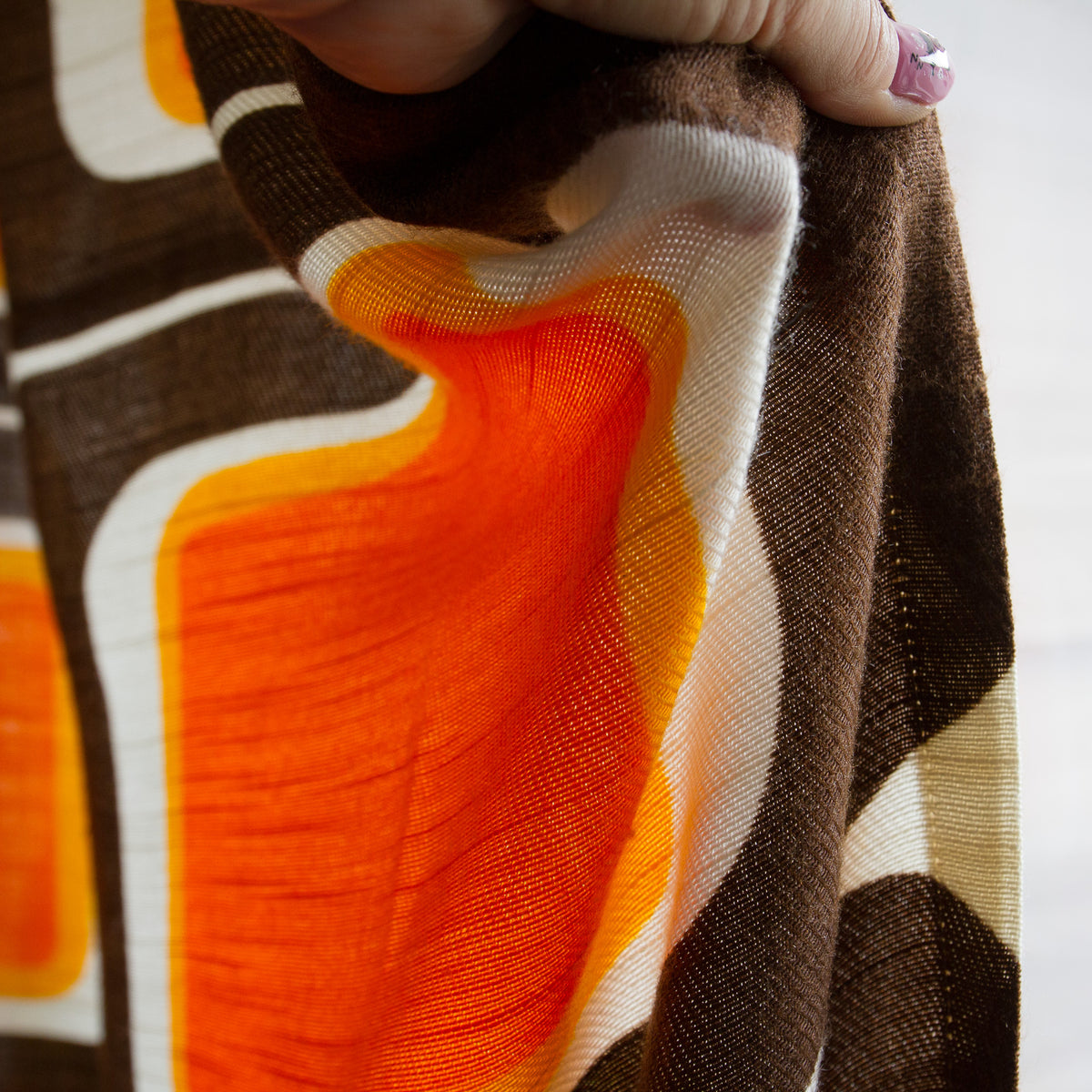 Hand holding vintage mid century curtain fabric showing the textured slub weave and printed brown pattern.