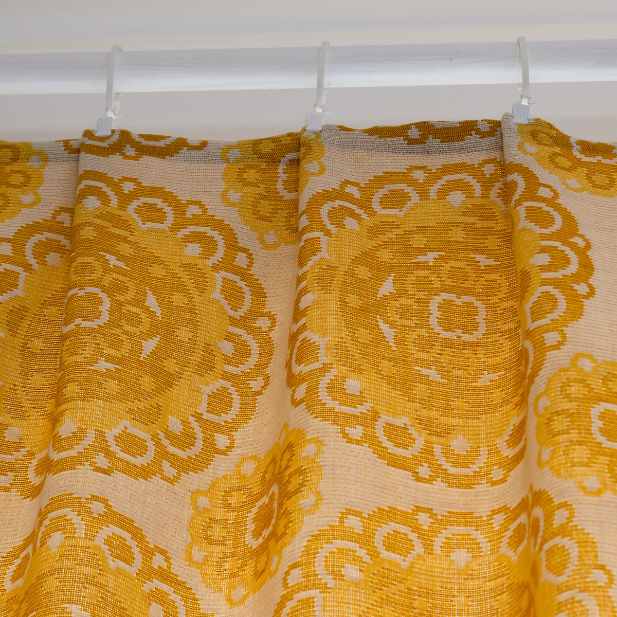 Top of vintage yellow drapes gathered with pleat tape and hanging on white curtain clips