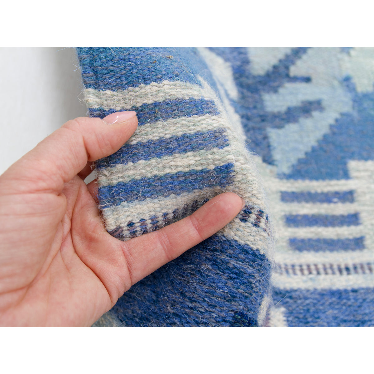 Hand holding the neat edge of the tapestry, to show the softness and density of the flatwoven wool rug.