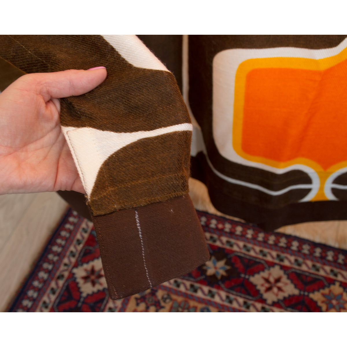 Neatly hemmed bottom detail of vintage brown and orange mid century drape, finished edge.