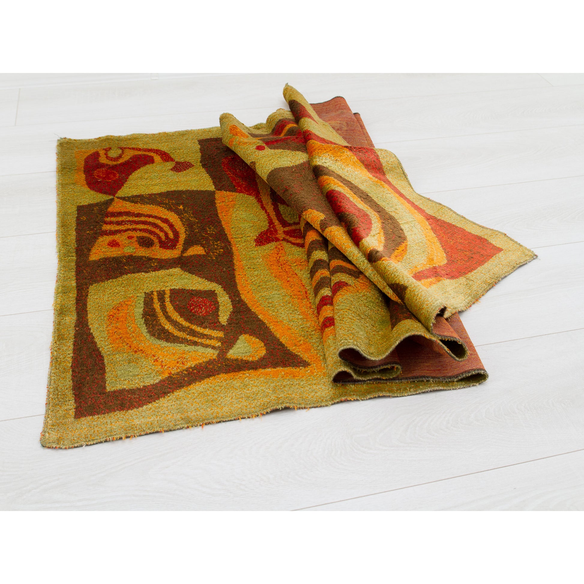 Angled view of the tapestry folded into soft waves on a white floor. Demonstrates the supple, pliable nature of the vintage fabric (not stiff or brittle) and the high-quality woven edge finish.