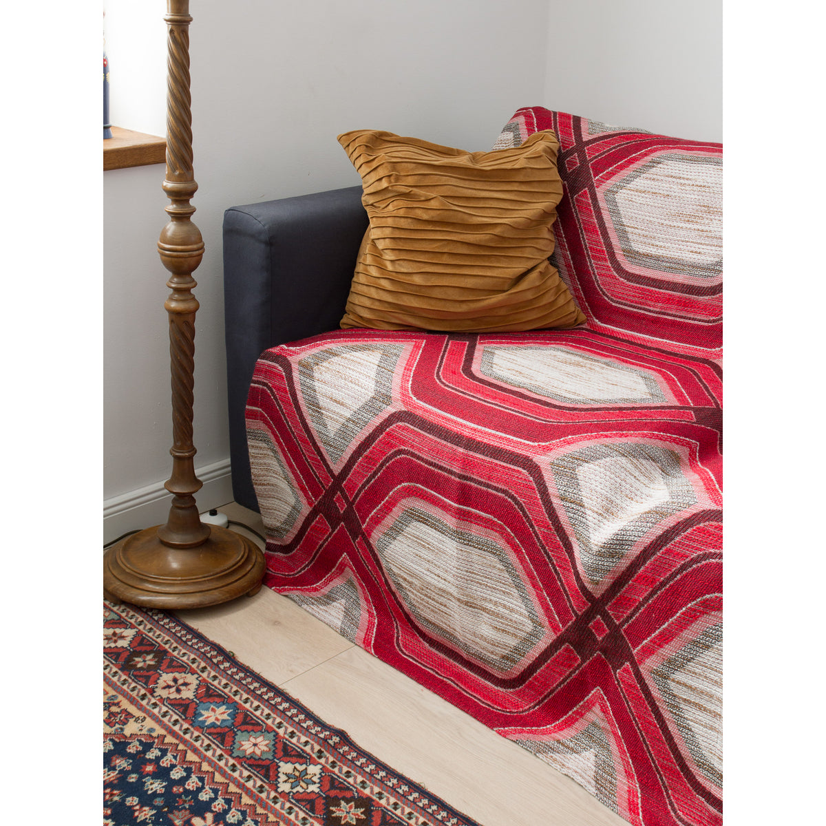 Vintage geometric woven fabric used as a sofa cover or bed throw in a retro 70s style living room, accented with a mustard yellow cushion