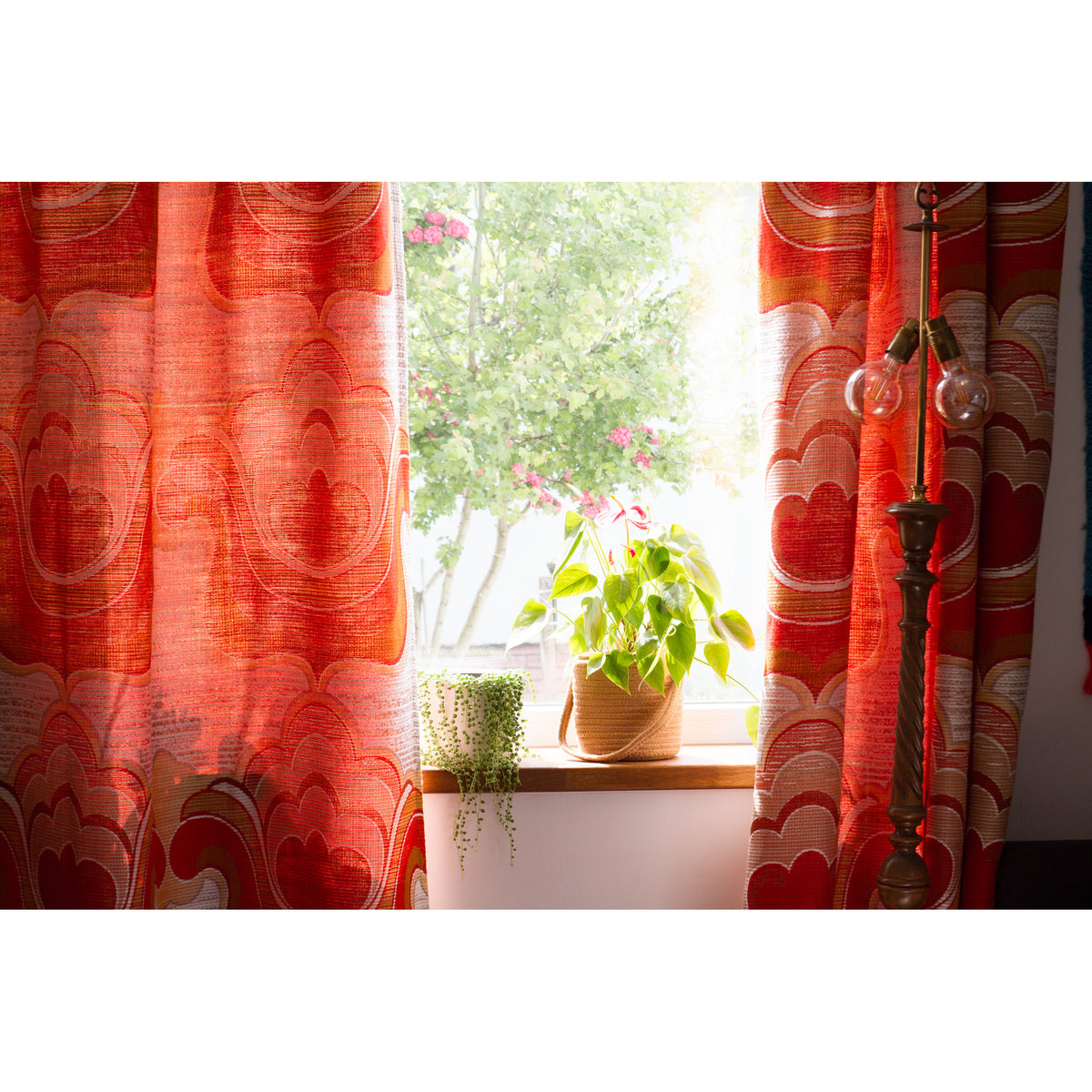 Two heavy vintage drapes on both sides of a sunny window, light filtering through the orange and red woven fabric