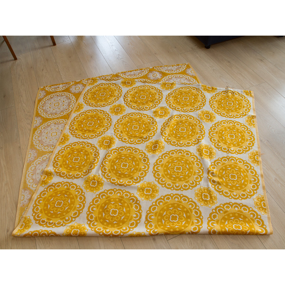 Vintage jacquard drapes folded on a light wooden floor, showing yellow and cream woven medallion textile