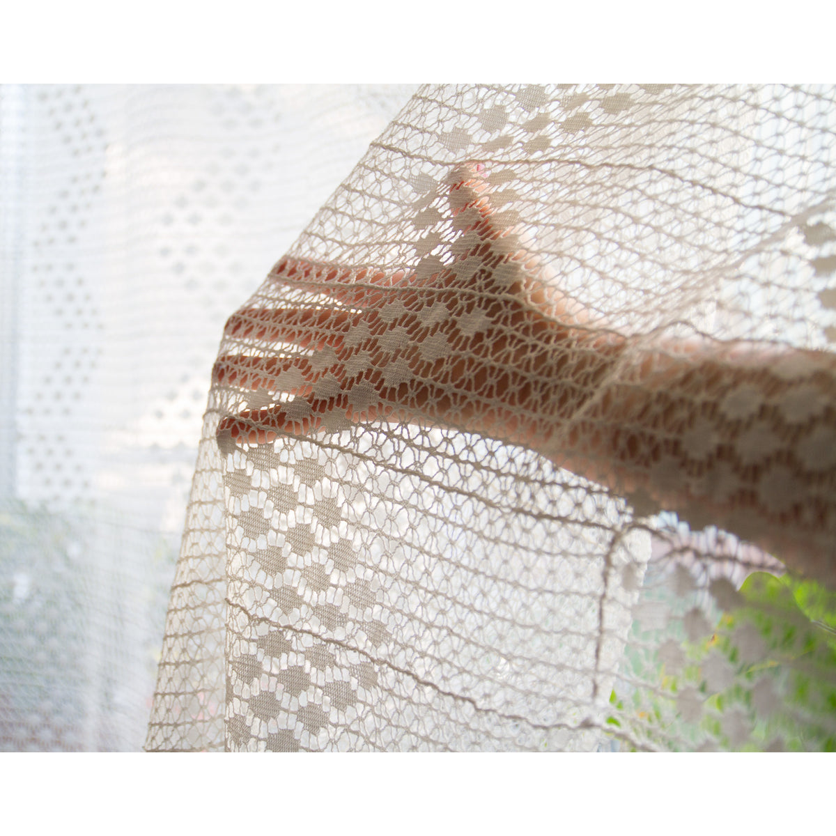 Hand behind vintage cream lace showing the diamond and flower crochet pattern