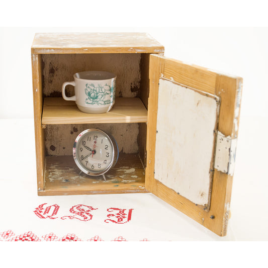 Small vintage mirror wall cabinet with its door open, displaying a white ceramic mug and a vintage alarm clock inside for scale. 