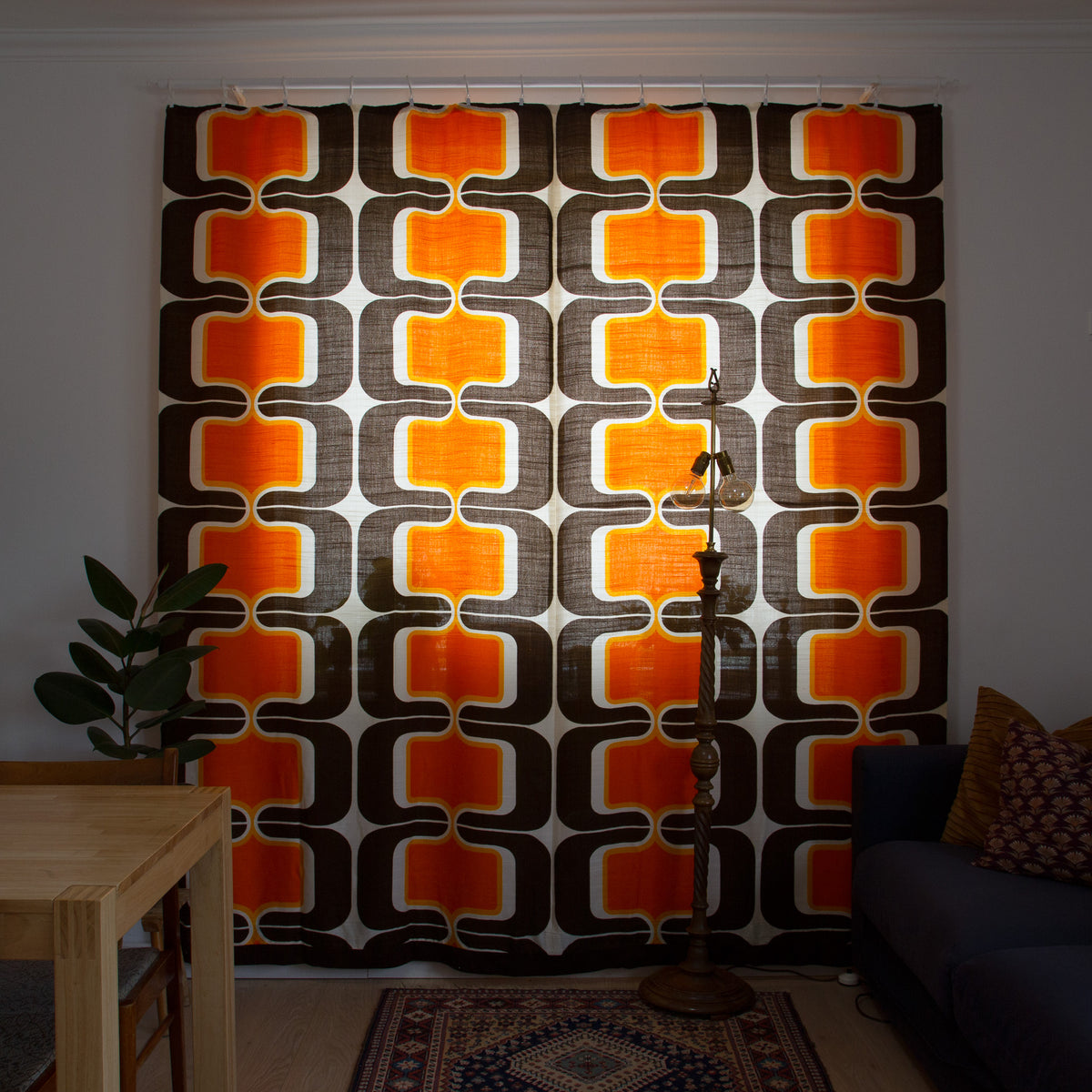 Pair of original 1960s vintage curtains with bold orange, brown and cream geometric pattern hanging in a bright living room, creating a perfect mid century interior.