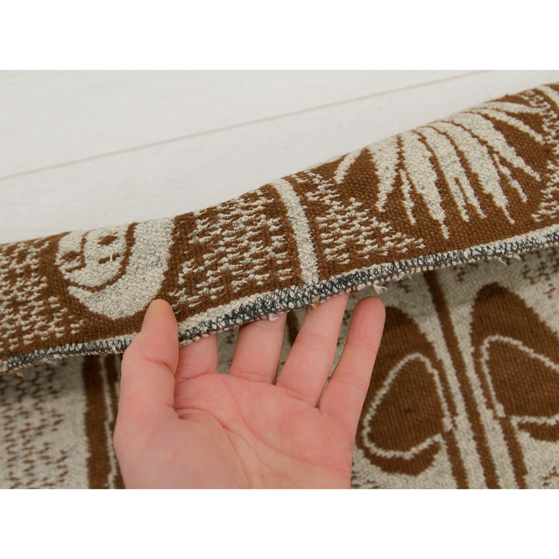 Hand holding the top edge of the tapestry, revealing careful mending. This wabi-sabi patina on the fabric demonstrates the authentic, lived-in nature of the vintage textile.