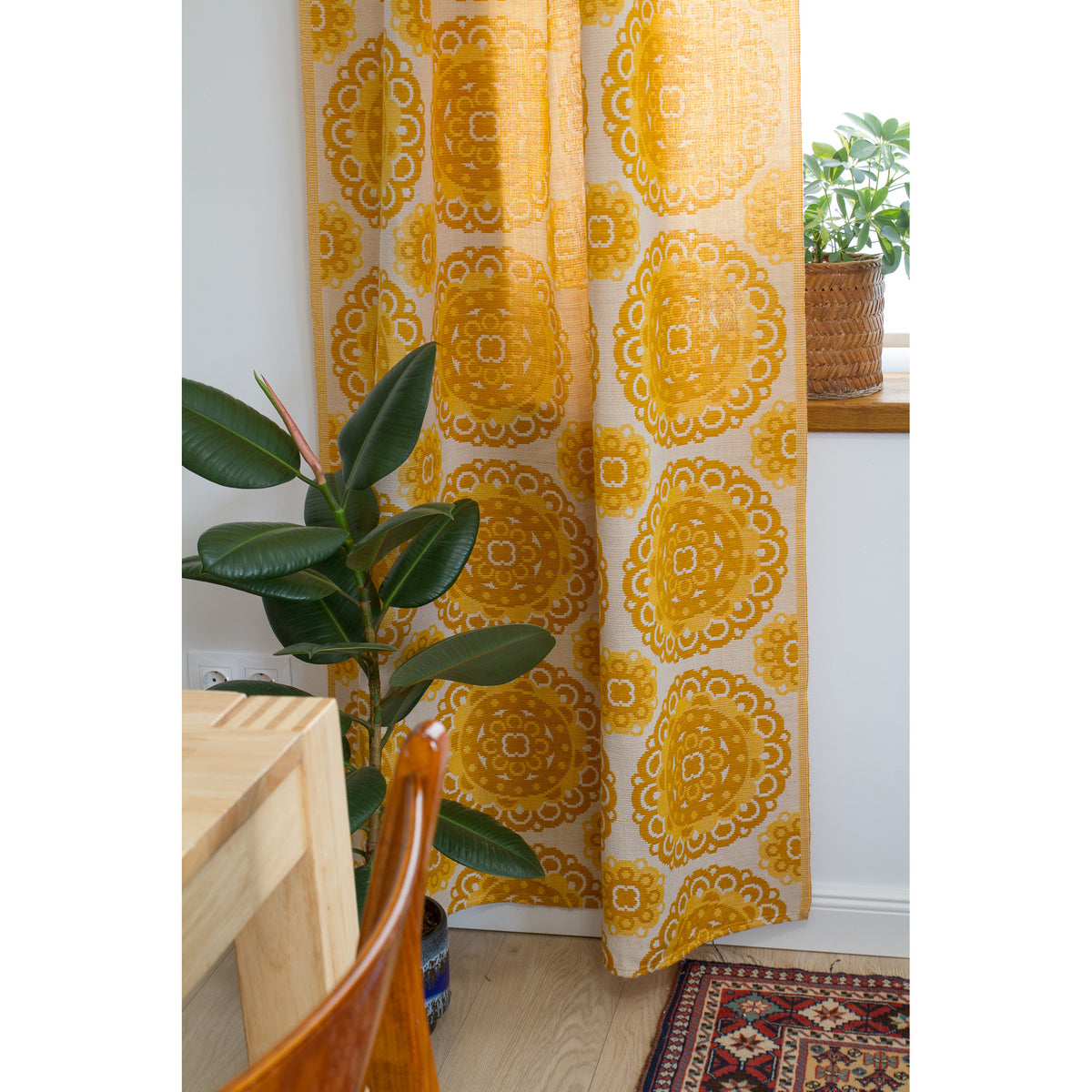 Full length mid century yellow curtain panel hanging next to a window with green plants and dining table