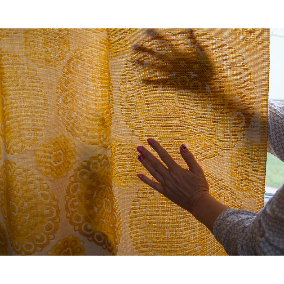 Sunlight shining through vintage mustard yellow jacquard curtain fabric, making the woven pattern glow warm golden.