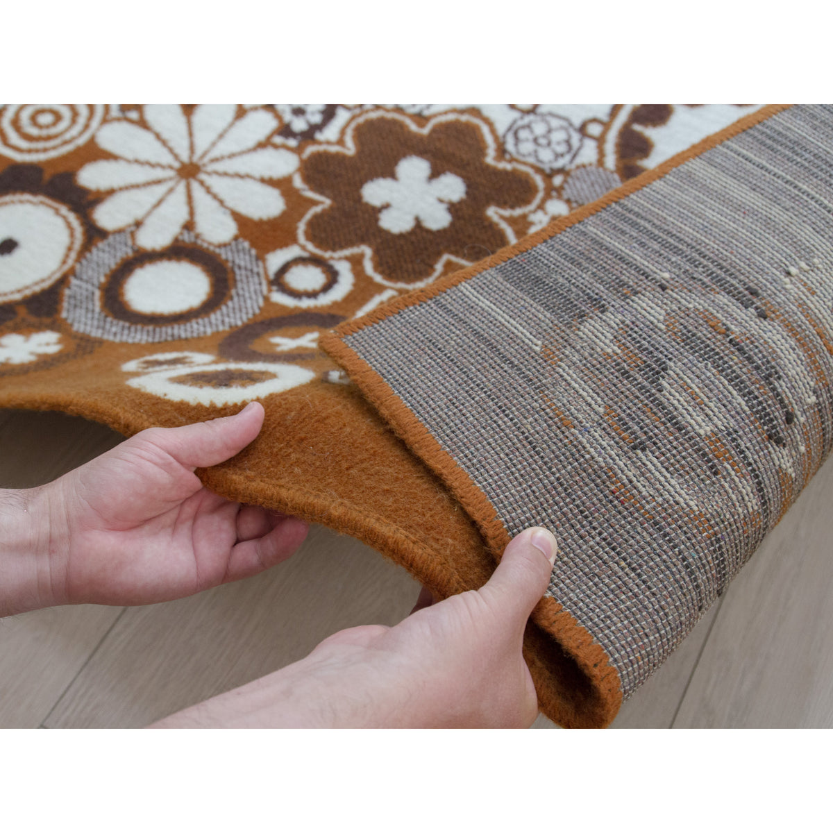 Hands holding the edge of vintage rug to show thickness and dense flat yet soft texture