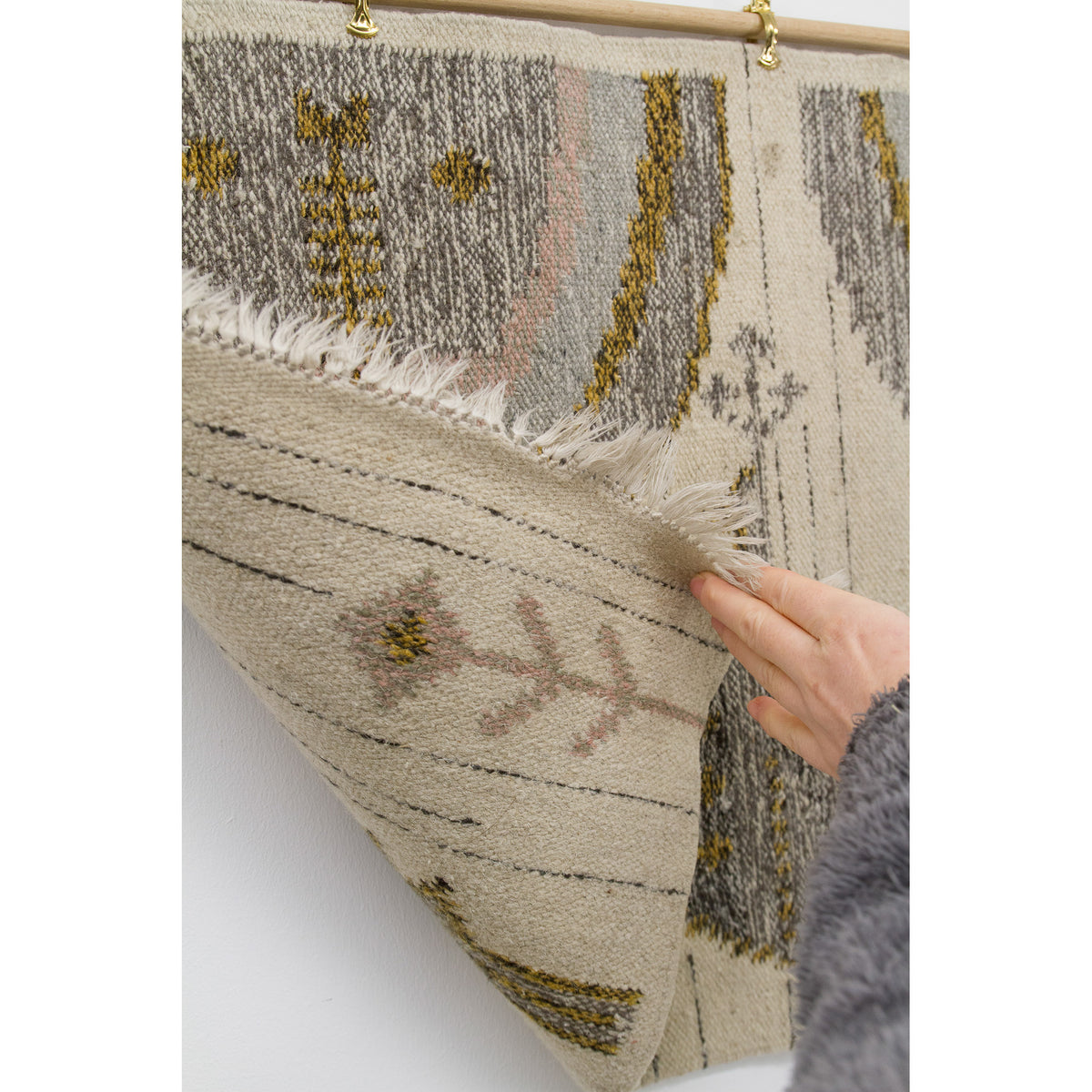 Hand lifting up the corner of the tapestry to reveal the clean, unfinished back. The pattern is visible in reverse, confirming the authenticity of the handwoven technique used in this vintage Hungarian folk art piece.