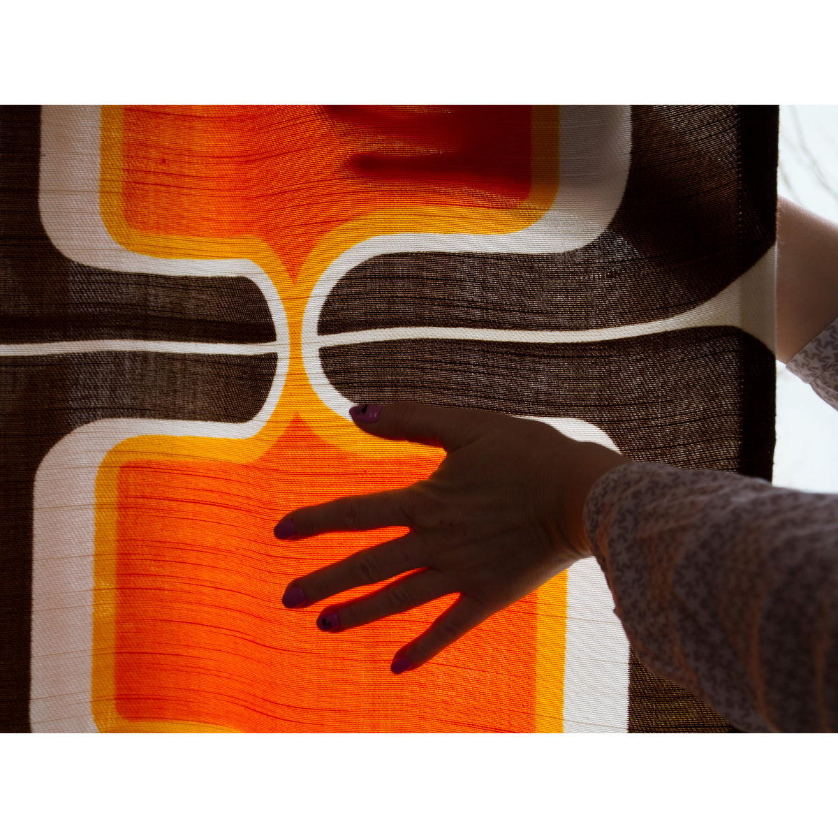 Sunlight shining through semi-sheer vintage cotton curtain making the retro orange pattern glow.