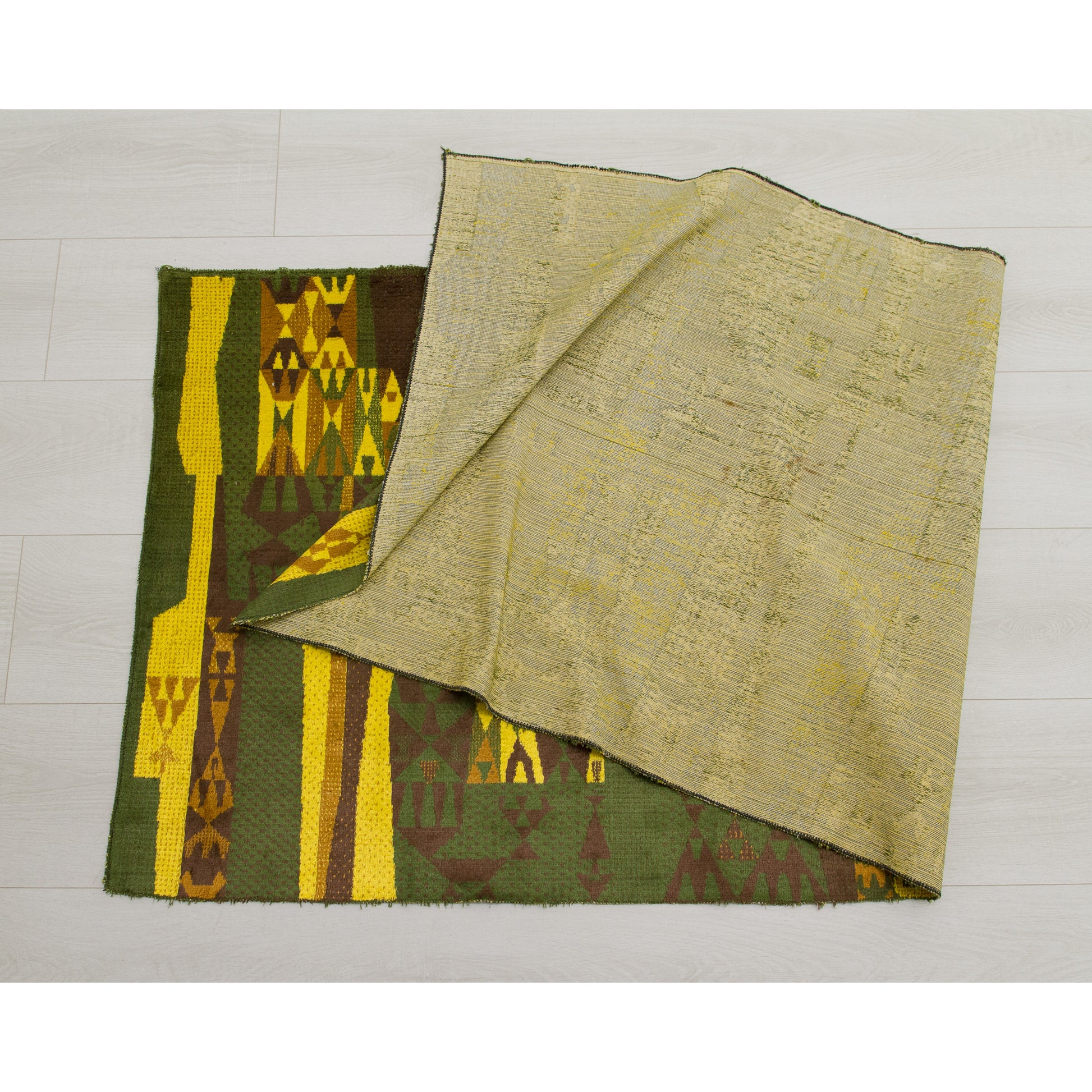 Flat view of the tapestry being folded, with  reverse side visible. Clean, woven backing showing the structure of the geometric pattern in negative.