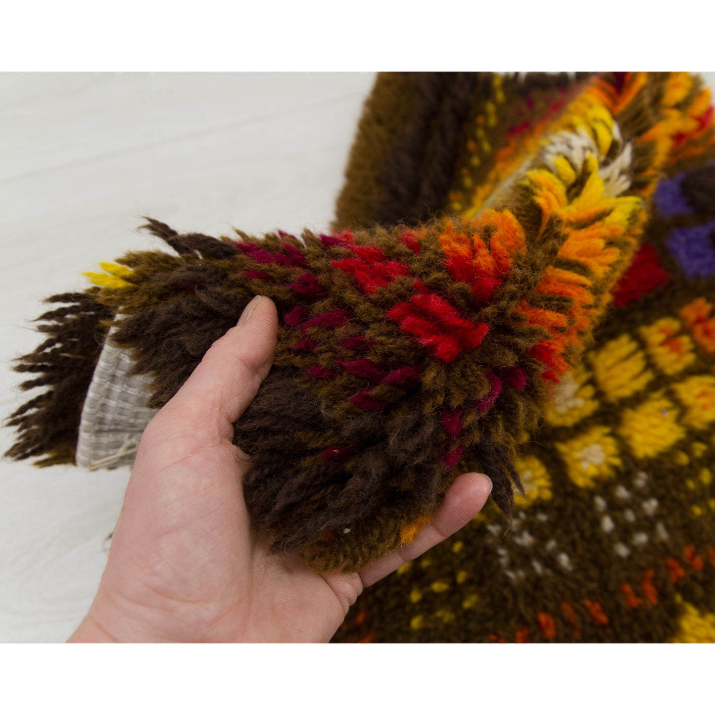The edge of the retro wall hanging is lifted and folded slightly in a hand, showing the superb thickness of the shag piles and high-quality European craftsmanship.