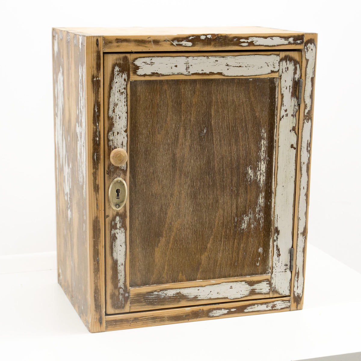Small vintage wall cabinet, refurbished and ready to use: a rustic wooden cabinet with a distressed finish, featuring peeling white paint on a brown wood base, a round wooden knob, and a brass keyhole, set against a plain white background.
