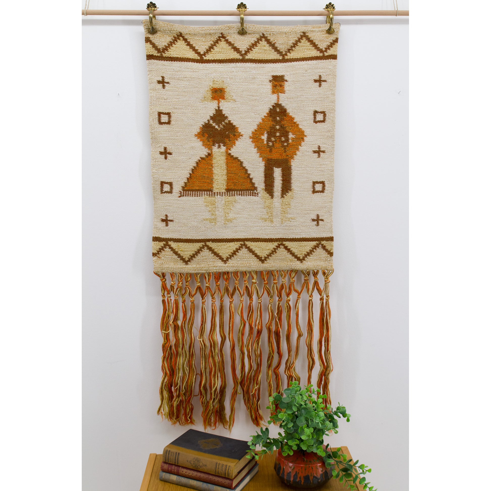 Full view of an authentic 1970s Hungarian wool tapestry hanging on a wall, showing a stylized abstract couple in beautiful rustic orange and brown tones.