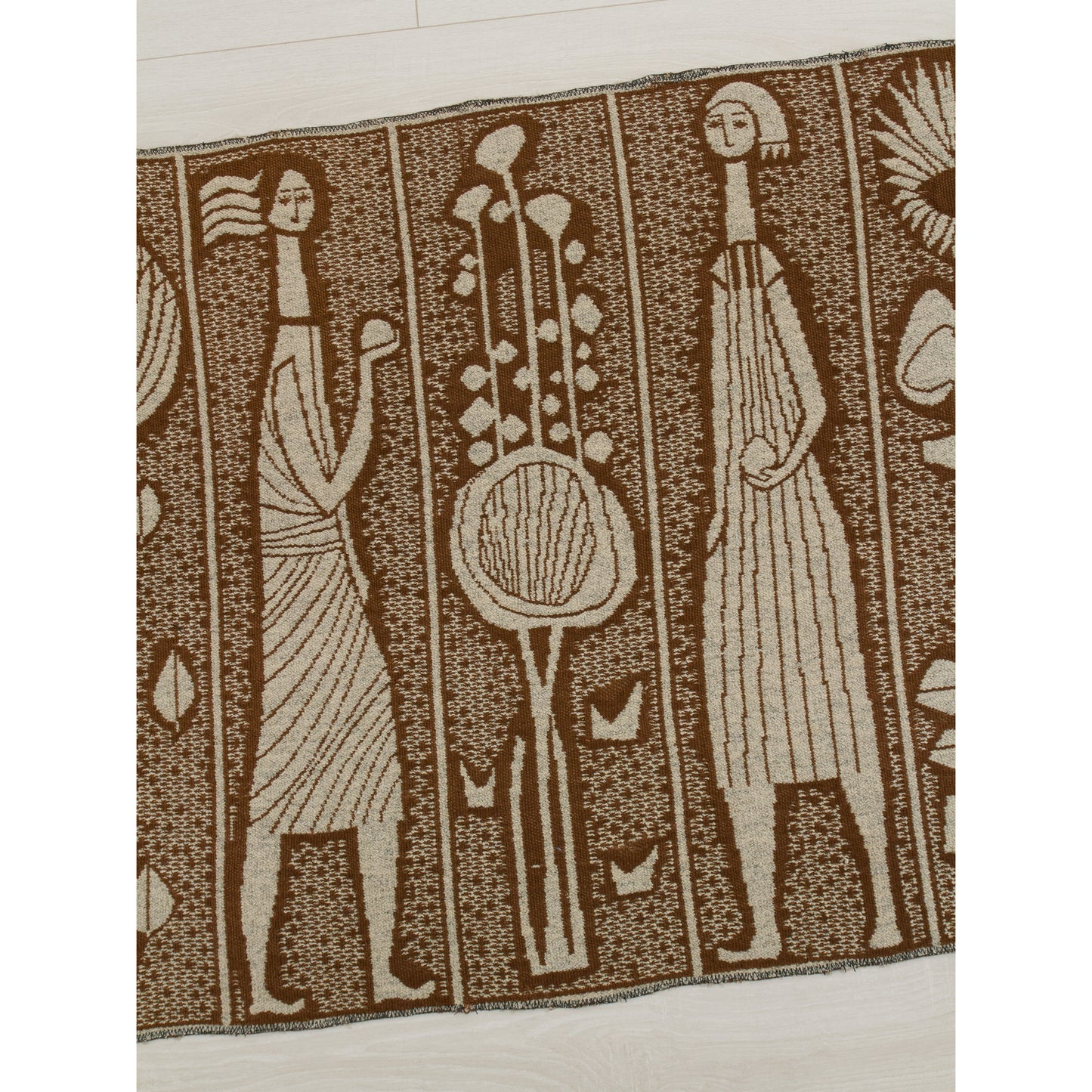 Close-up of the mid century modern tapestry's pattern featuring abstract female figures holding objects, alternating with large stylized sun-flowers or thistle motifs. The geometric yet organic design reflects the 1960s modernist style.