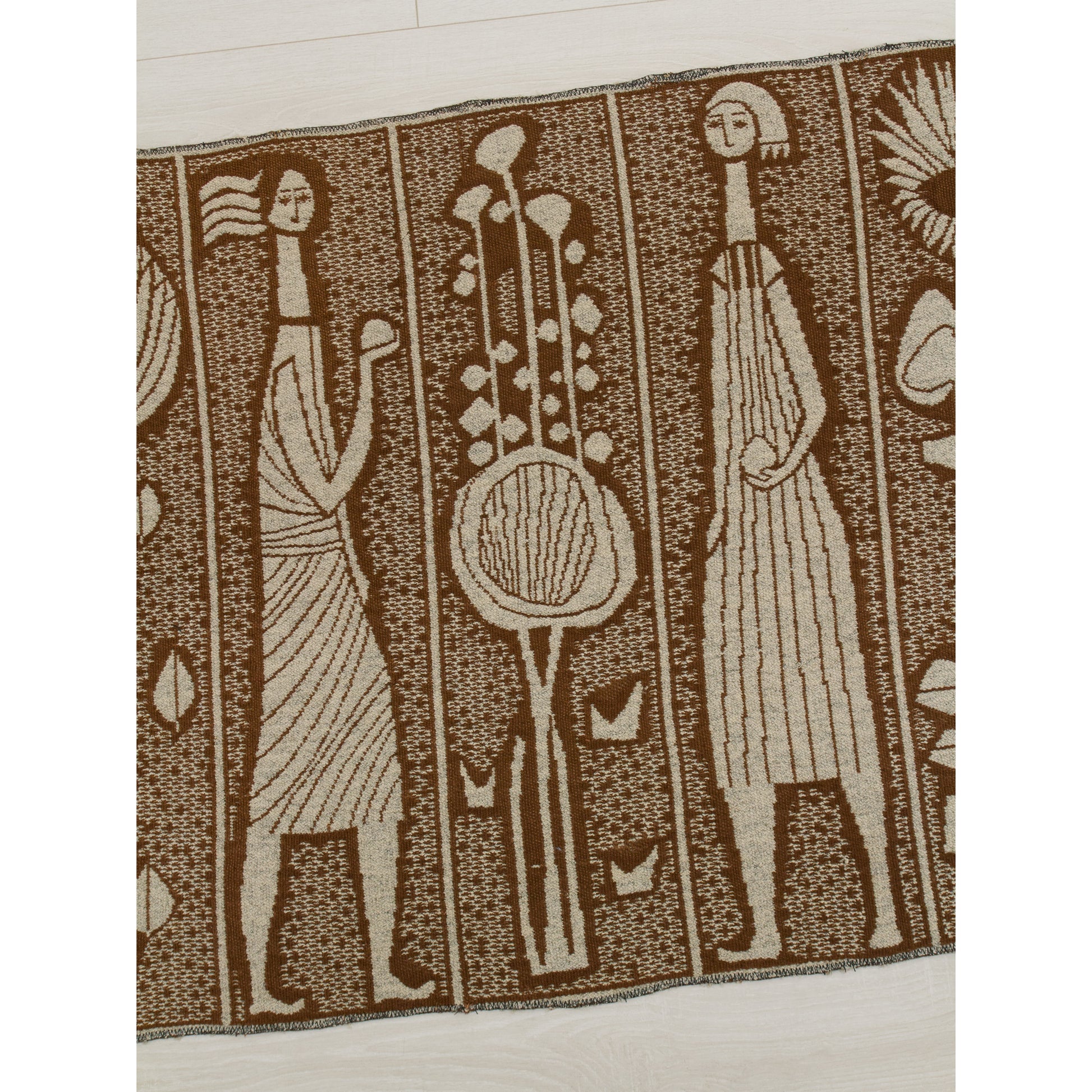 Close-up of the mid century modern tapestry's pattern featuring abstract female figures holding objects, alternating with large stylized sun-flowers or thistle motifs. The geometric yet organic design reflects the 1960s modernist style.