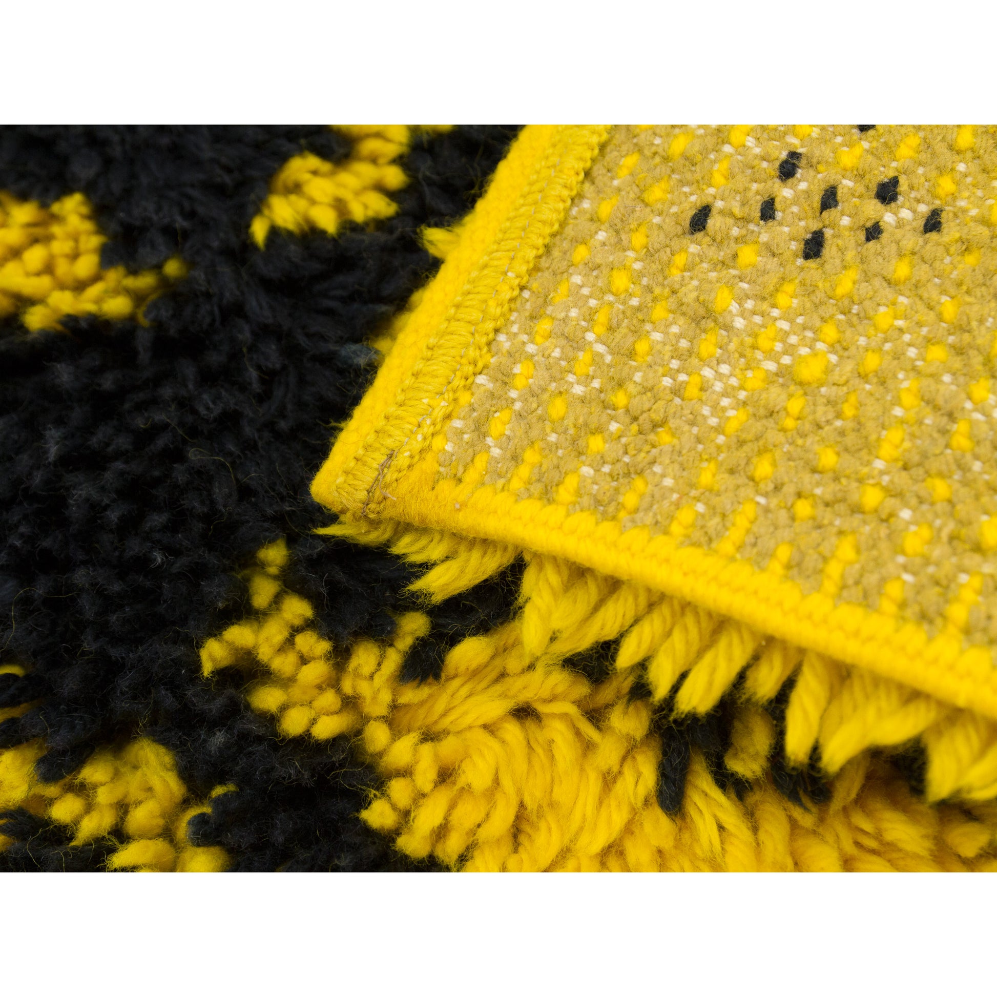 Extreme close-up of the corner of the rug folded back, showing both sides. Rich, extra chunky high piles on the surface in vivid yellow and black - on a heavy-duty woven foundation.