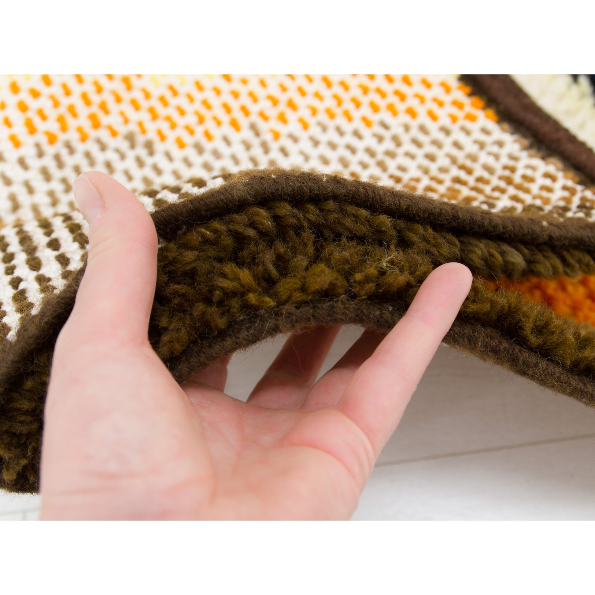 Woven hem detailing held in hand, demonstrating the excellent preserved craftsmanship of this thick shag rug.