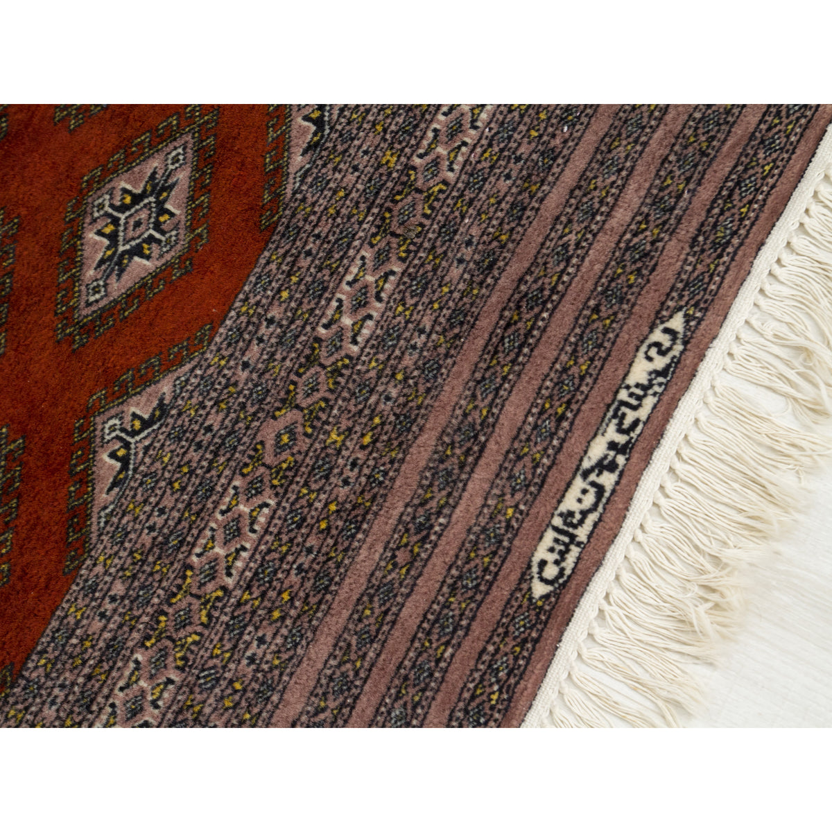 Woven signature in the border of a vintage Bokhara rug next to the cream fringe, as a sign of a skilled rug weaver